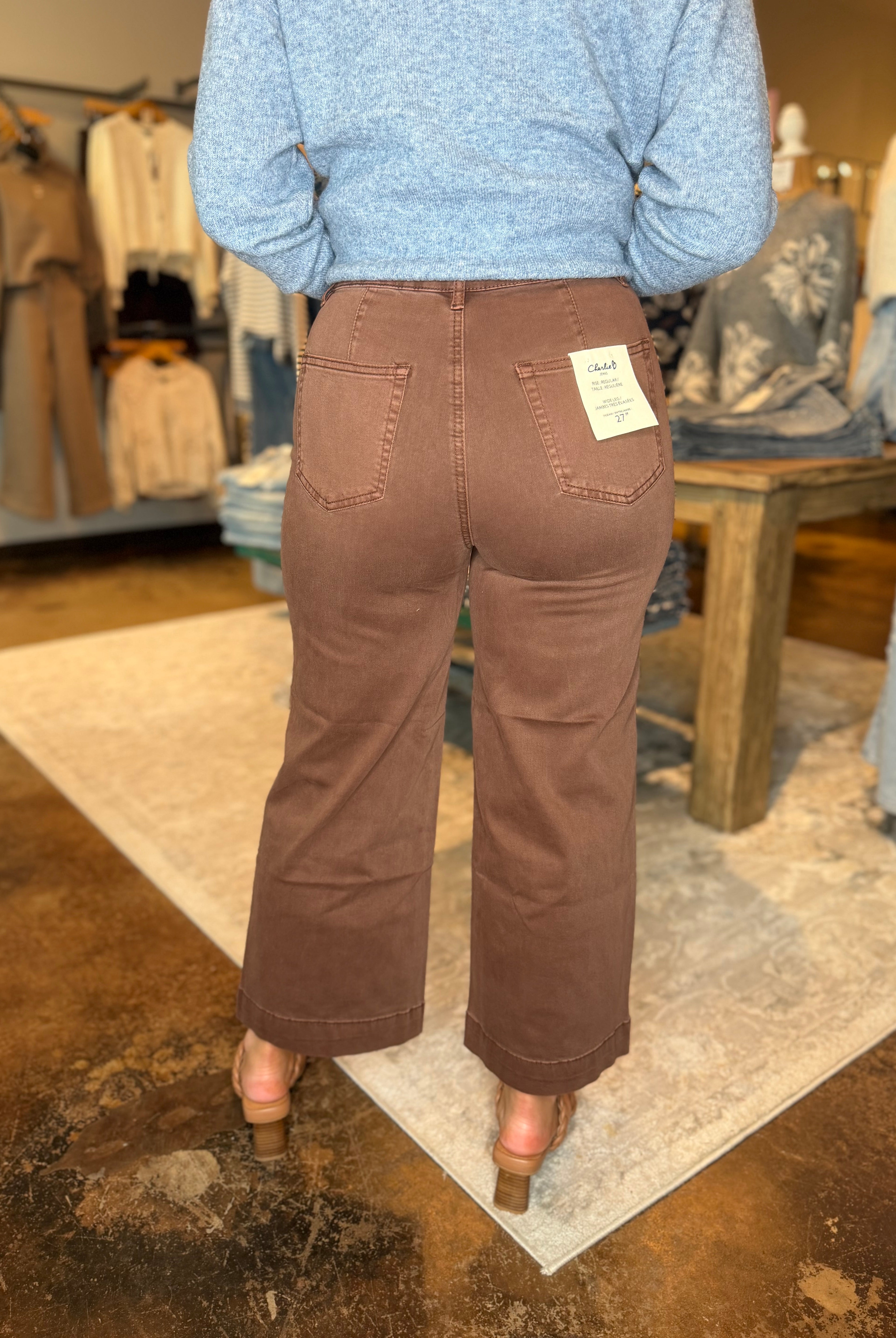 A person shown from the back wearing brown wide-leg cropped pants and a light blue heathered sweater in a clothing store.