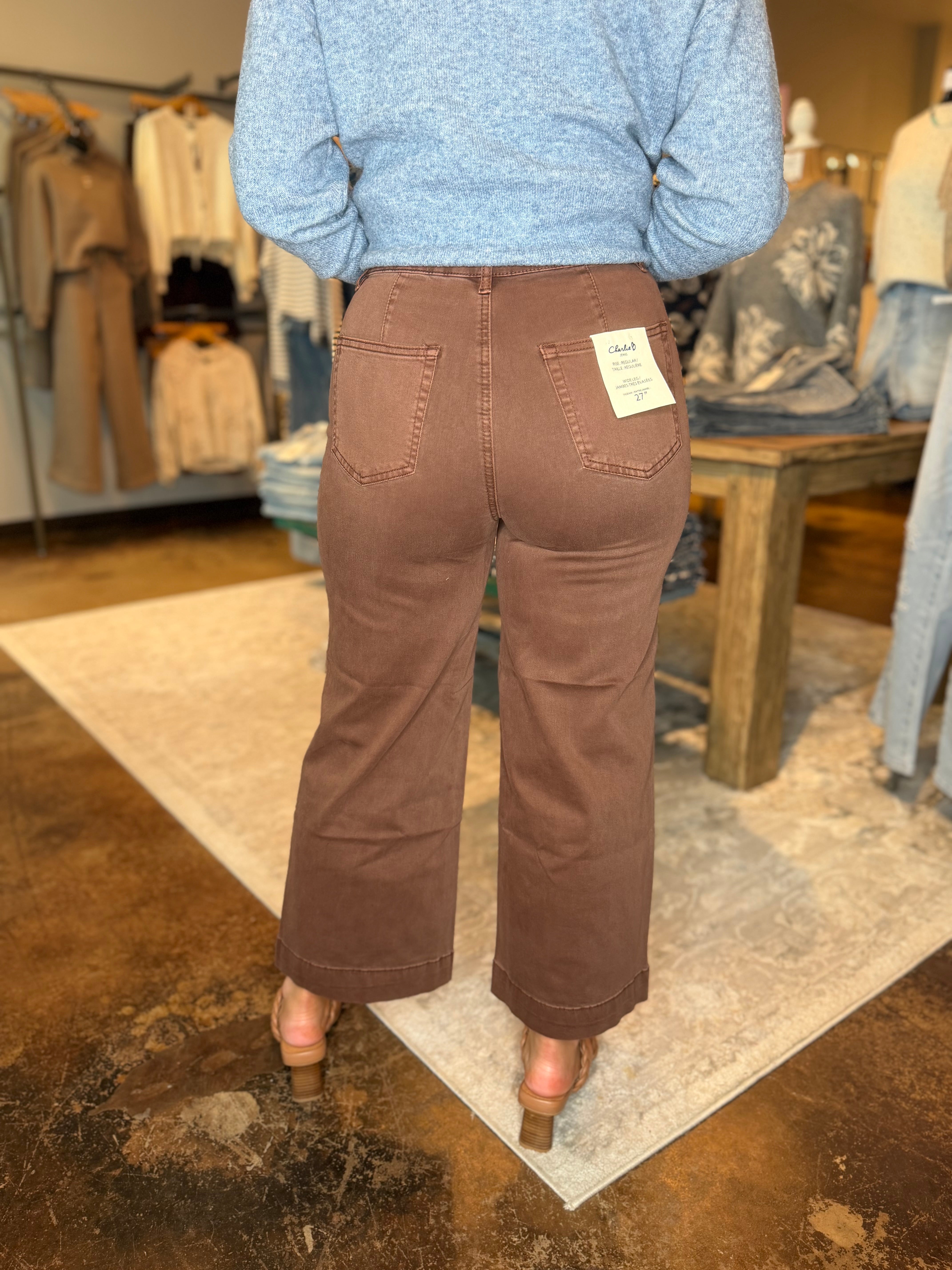 A person shown from the back wearing brown wide-leg cropped pants and a light blue heathered sweater in a clothing store.
