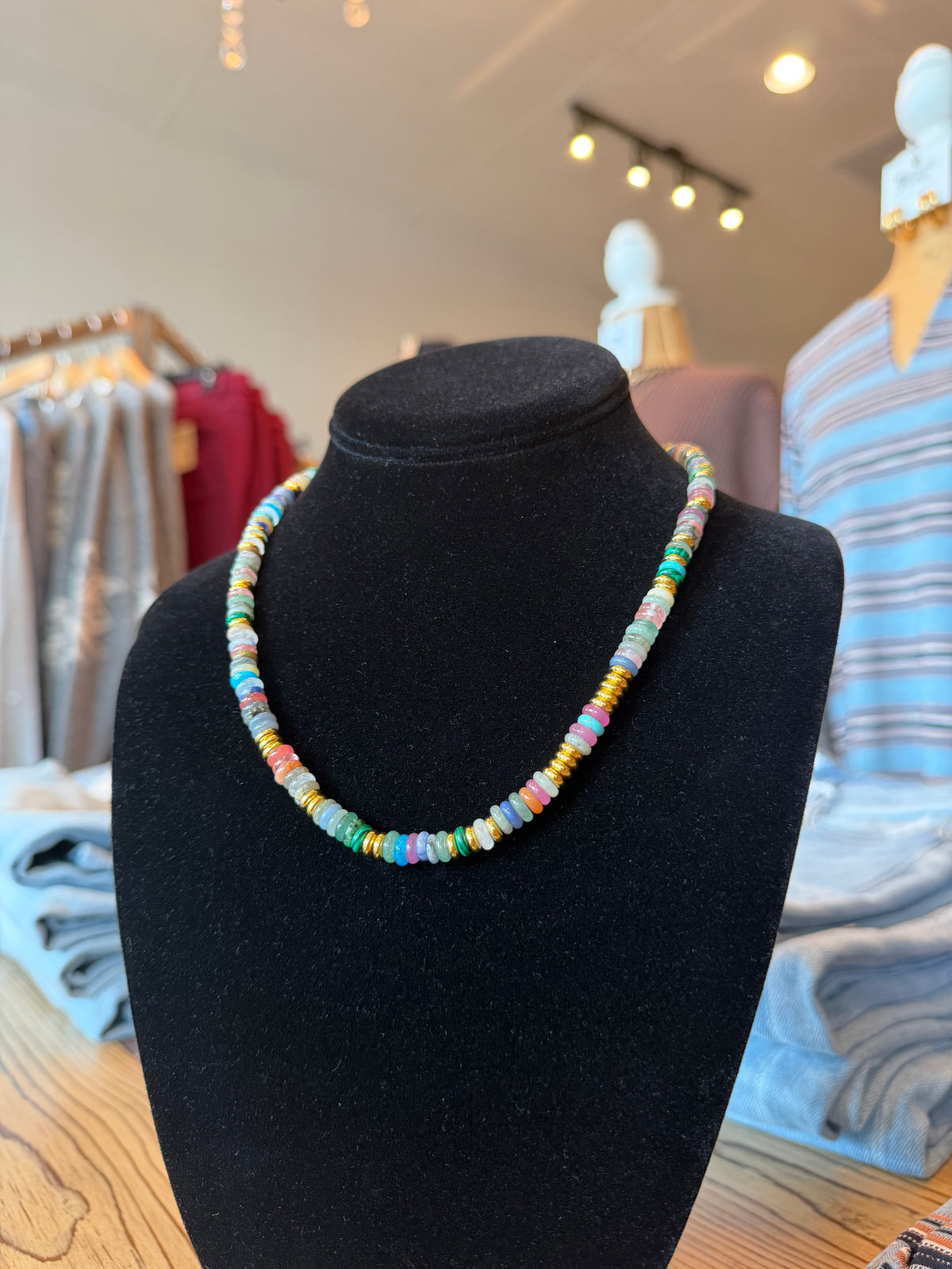 A colorful beaded necklace displayed on a black velvet jewelry bust in a retail store setting.