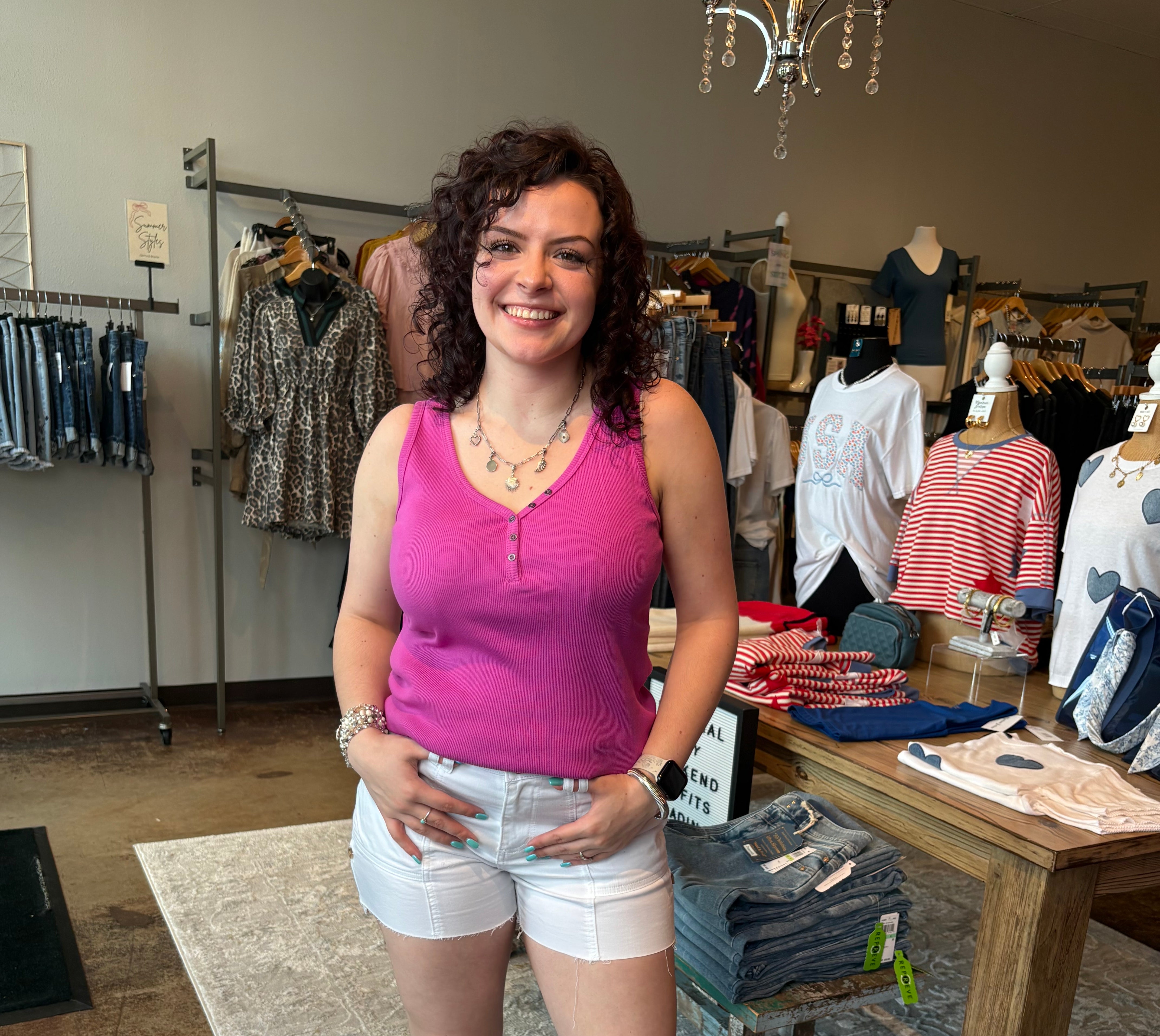 Woman in a pink tank top and white shorts standing in a clothing store.
