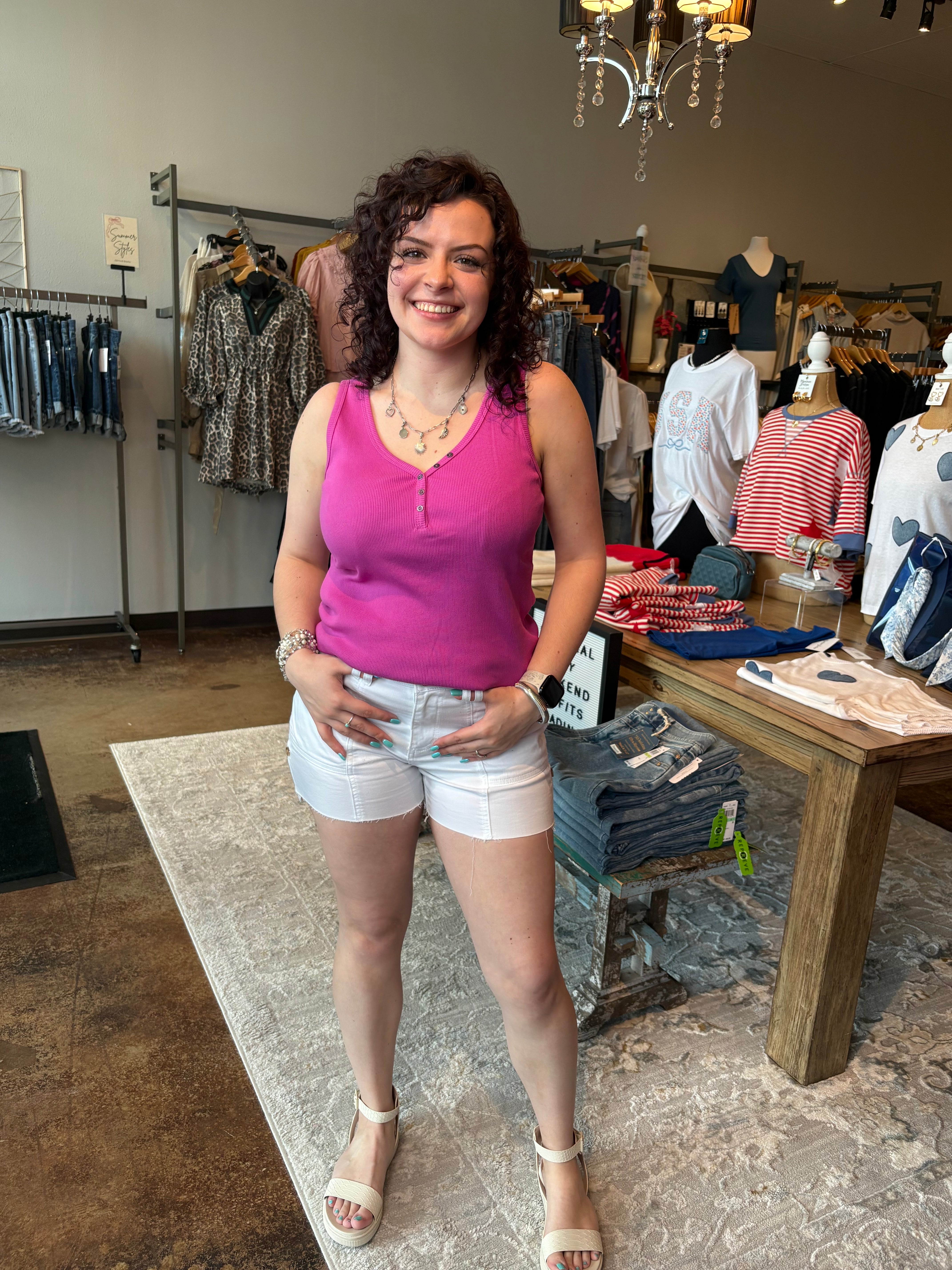 Woman in a pink tank top and white shorts standing in a clothing store.