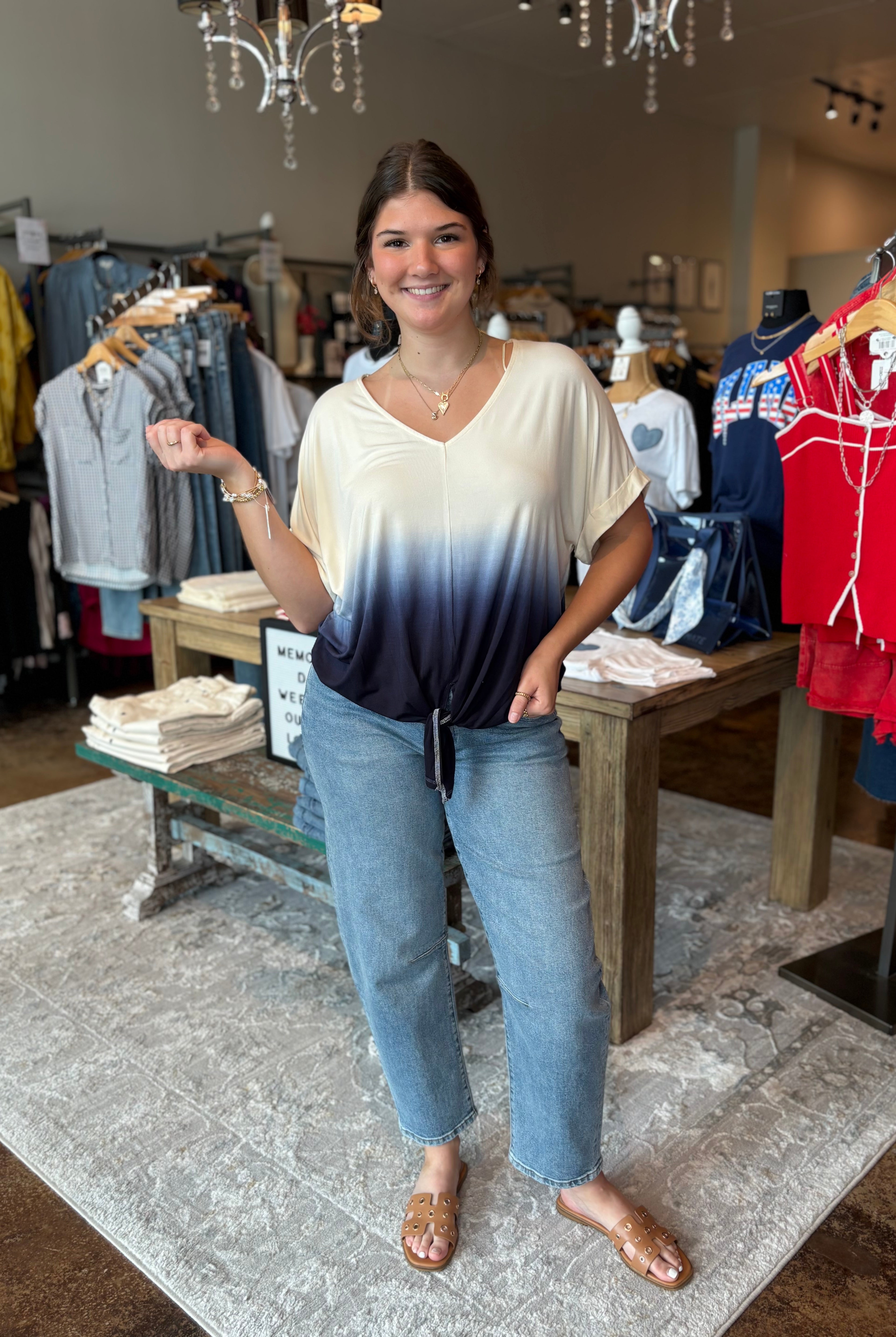 Woman standing in a clothing store wearing an ombre top and jeans.