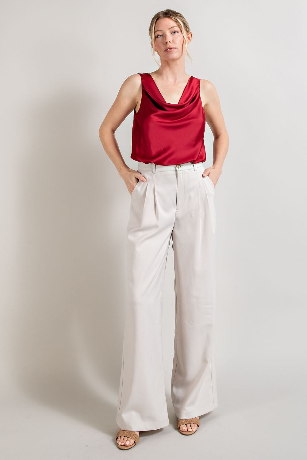 Woman wearing a red sleeveless top and white pants against a plain background
