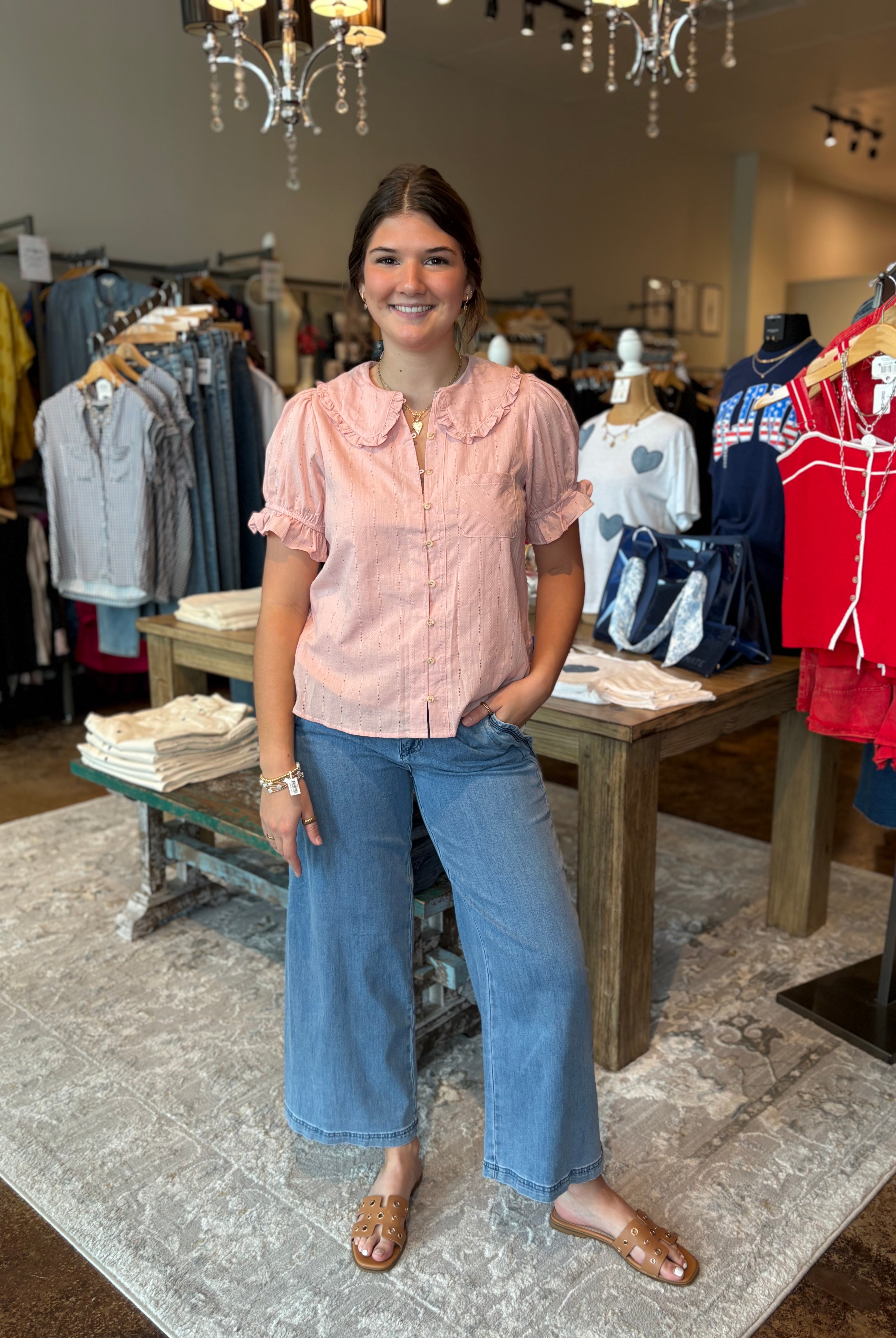 Woman in a pink shirt and blue jeans standing in a clothing store.