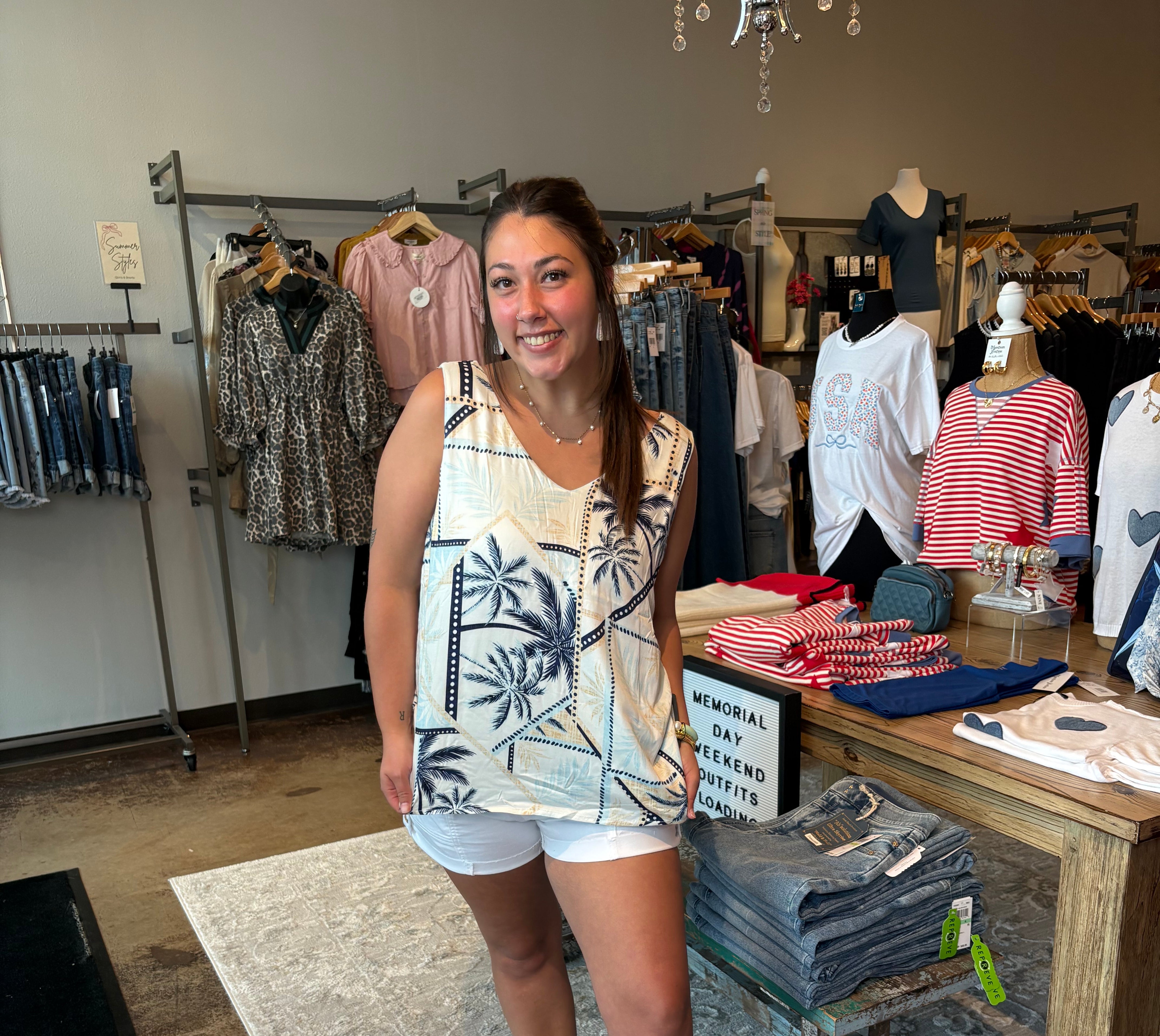 Woman standing in a clothing store wearing a sleeveless top and shorts.