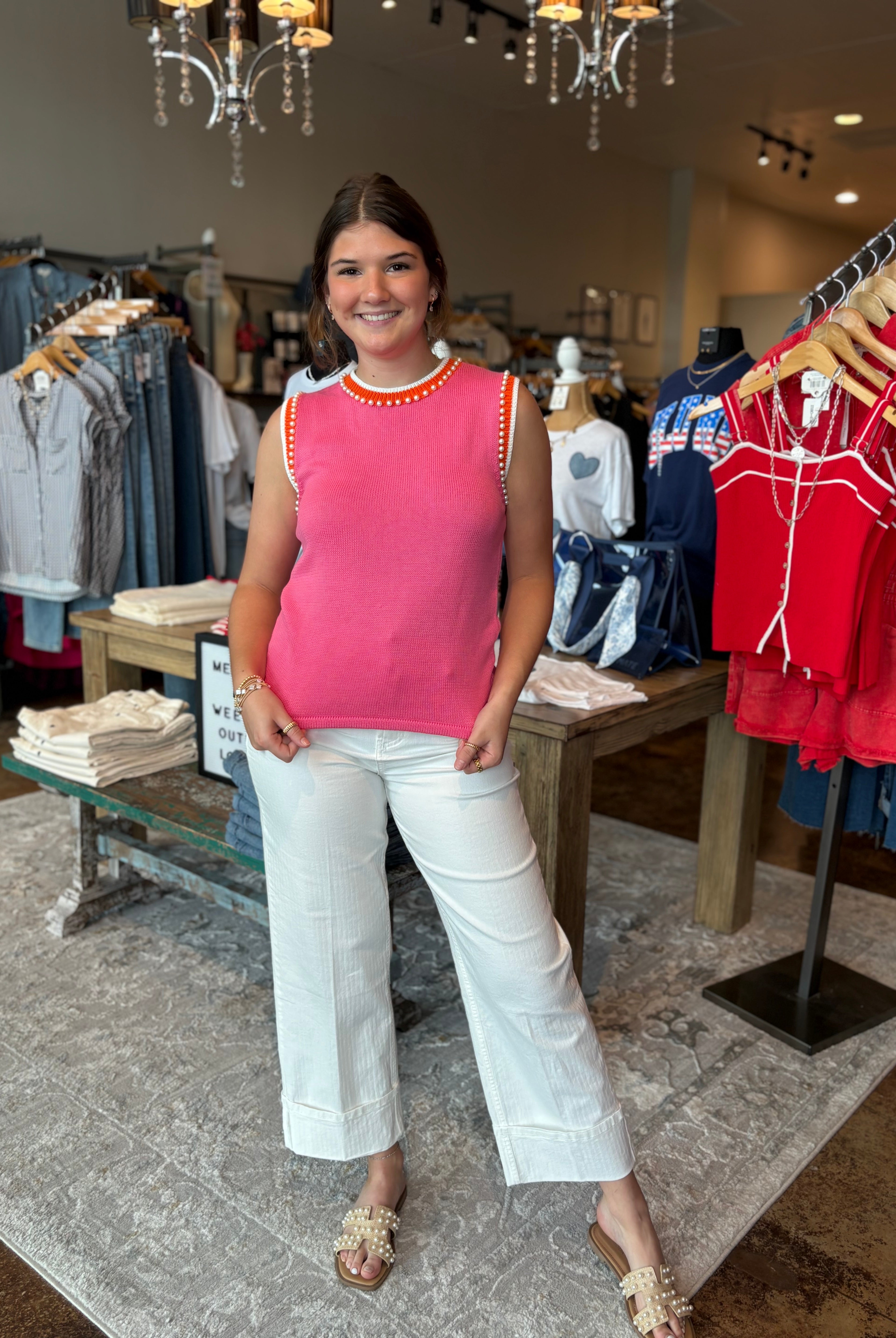 Woman wearing a pink top and white pants standing in a clothing store.