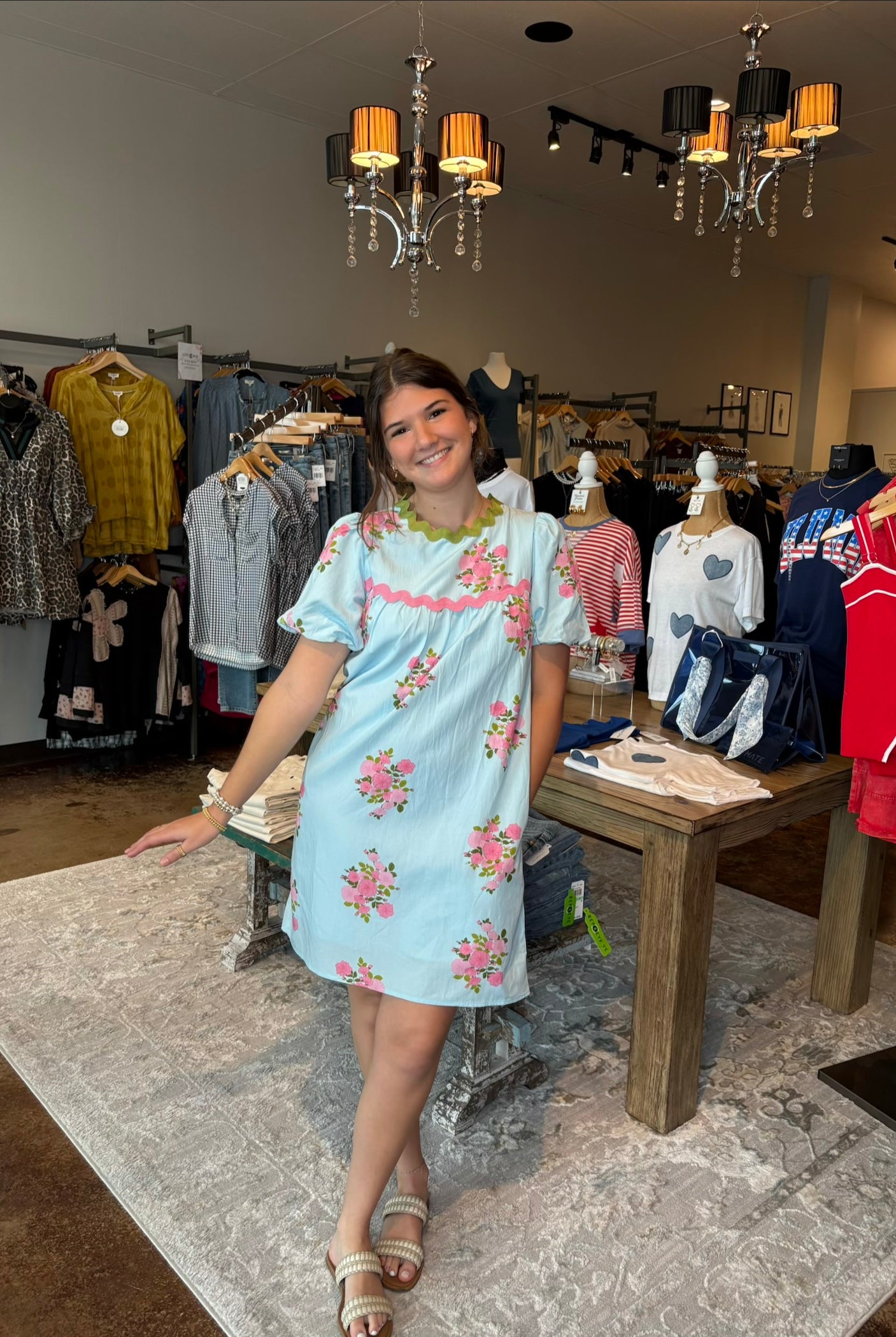 Young girl in a light blue floral dress standing in a clothing store.