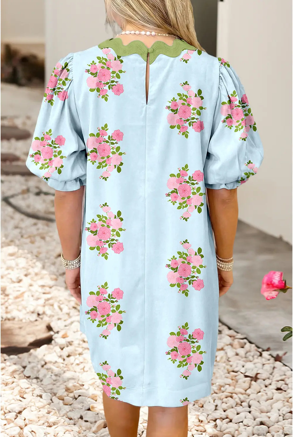 Light blue dress with pink floral patterns worn by a person, standing on pebbles.