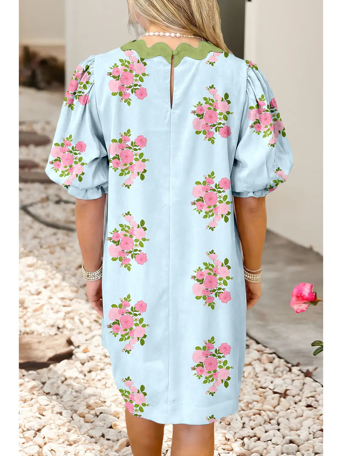 Light blue dress with pink floral patterns worn by a person, standing on pebbles.