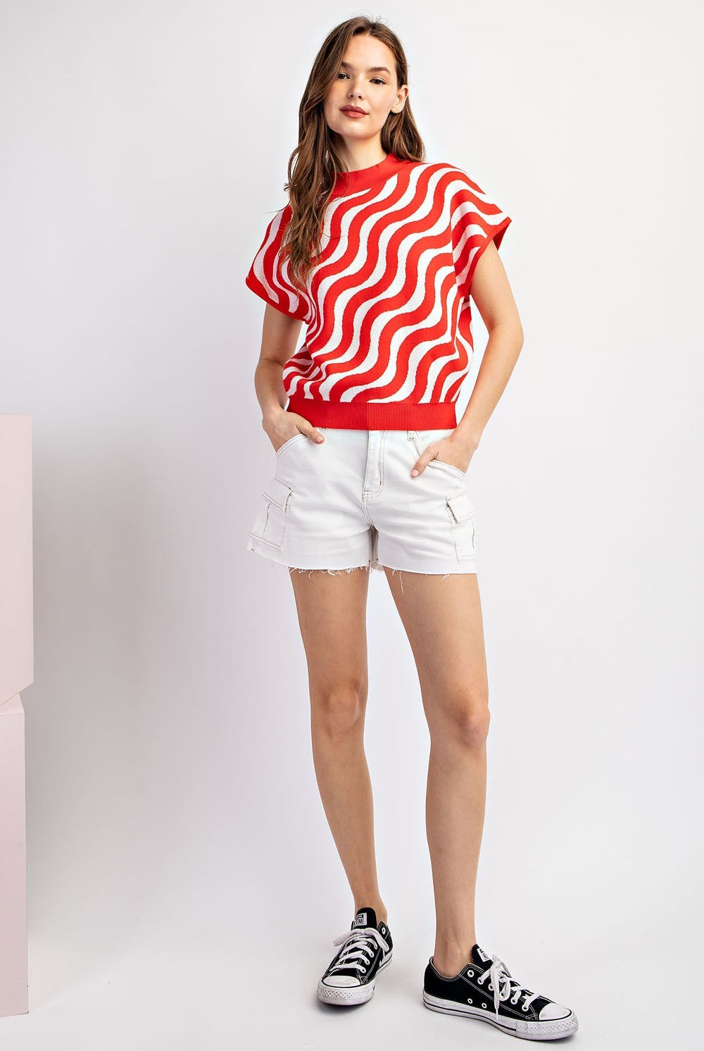 Woman wearing a red and white striped shirt with white shorts on a light gray background