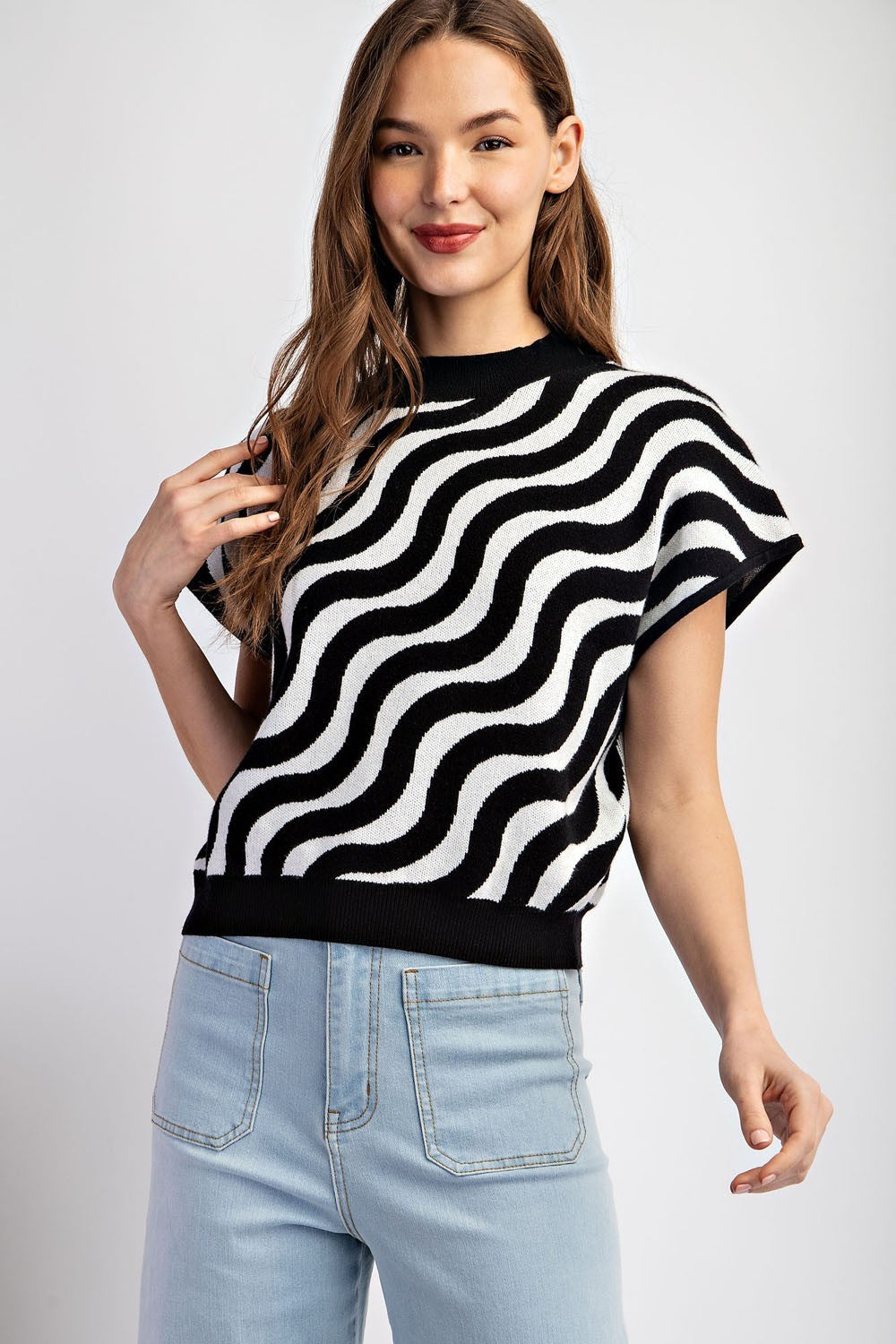 Woman wearing a black and white striped sweater with light blue jeans on a plain background