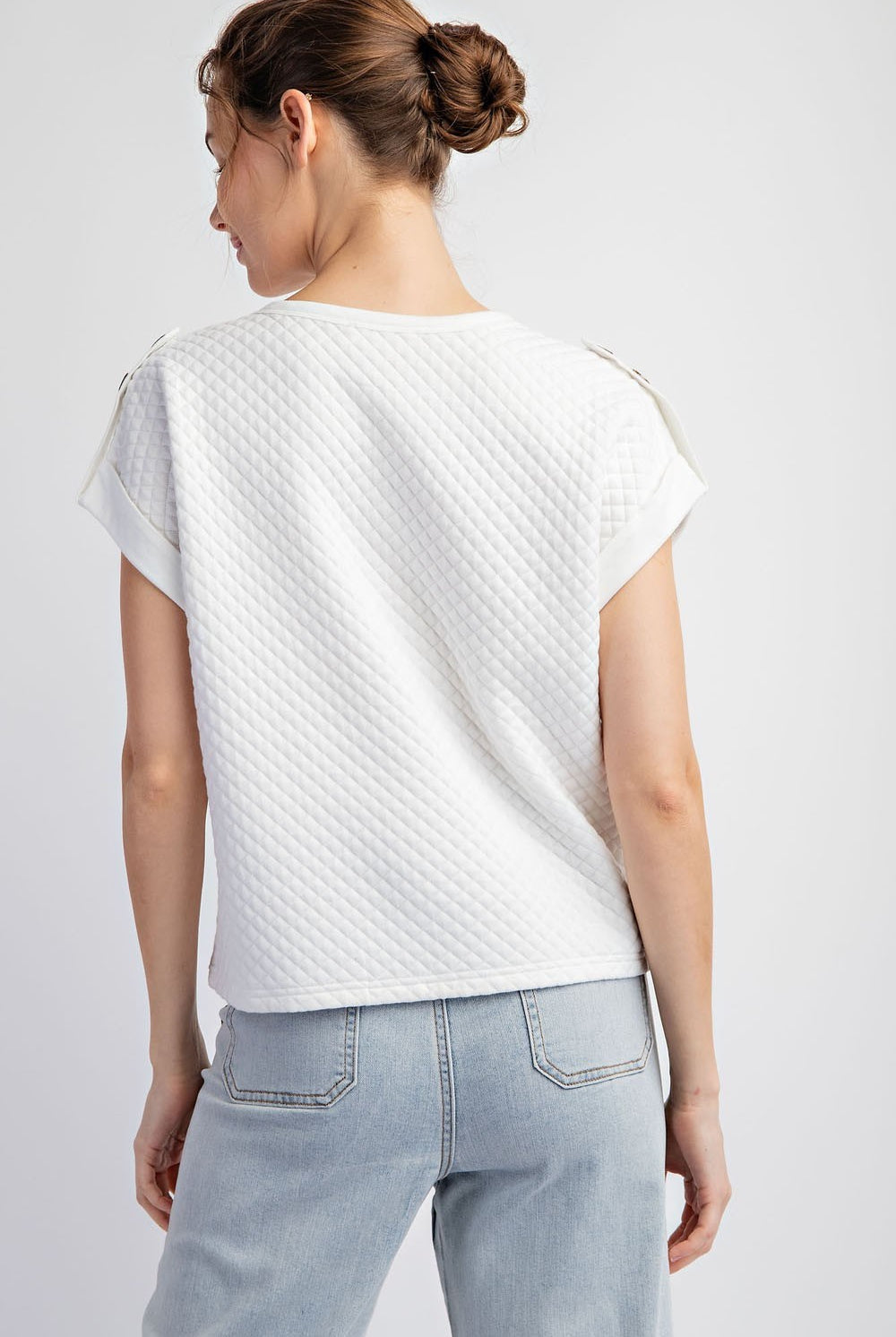 Woman wearing a textured white top and light blue jeans on a plain background