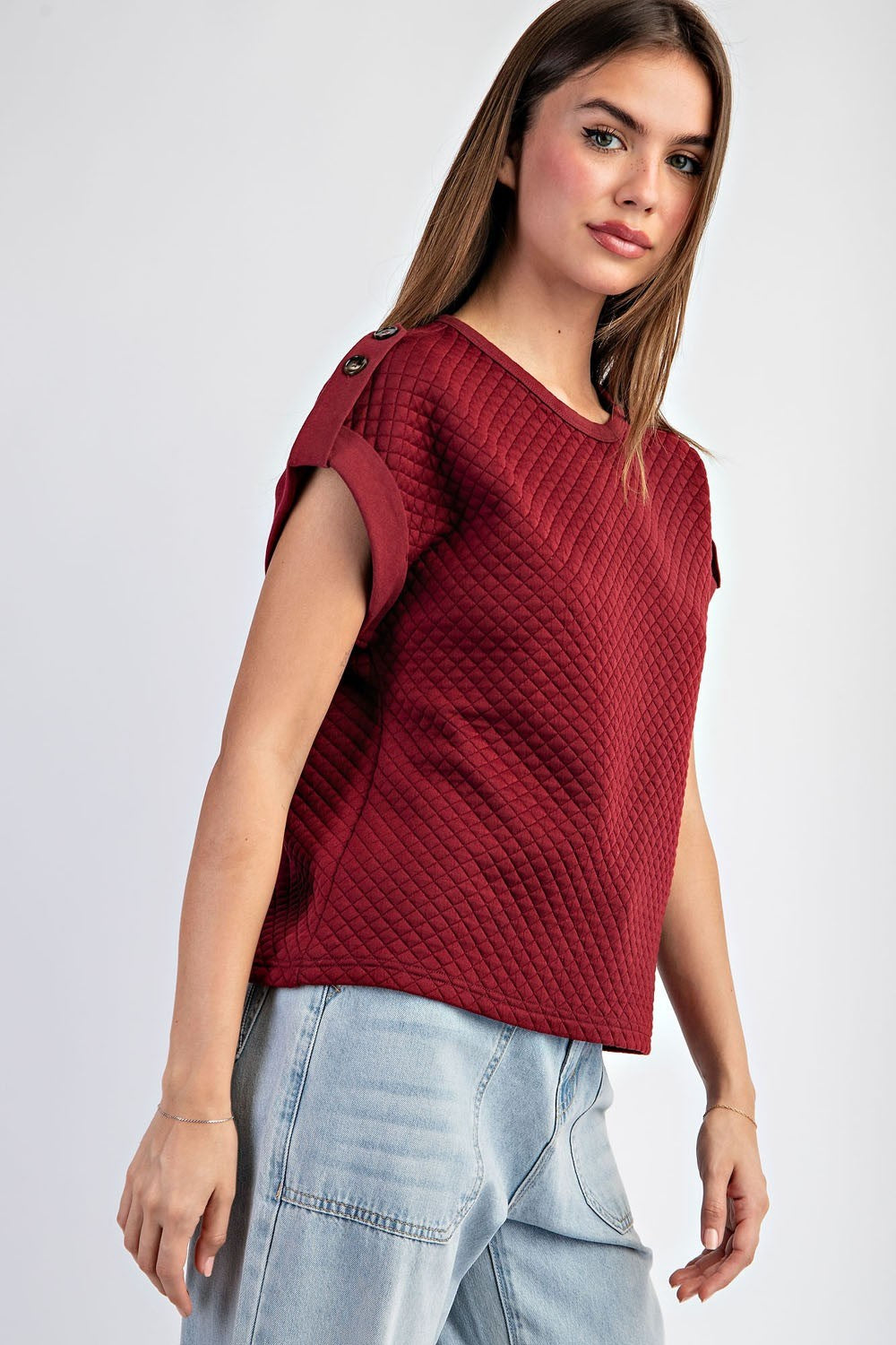 Woman wearing a red textured top and light blue jeans on a white background