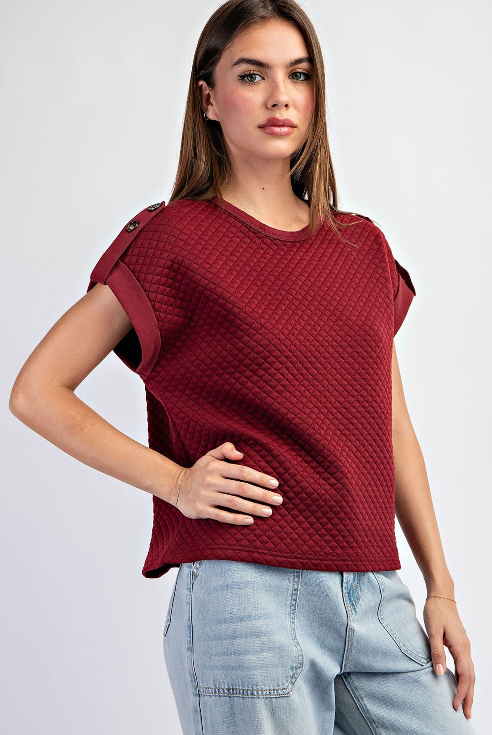 Woman wearing a textured red top and light blue jeans on a white background