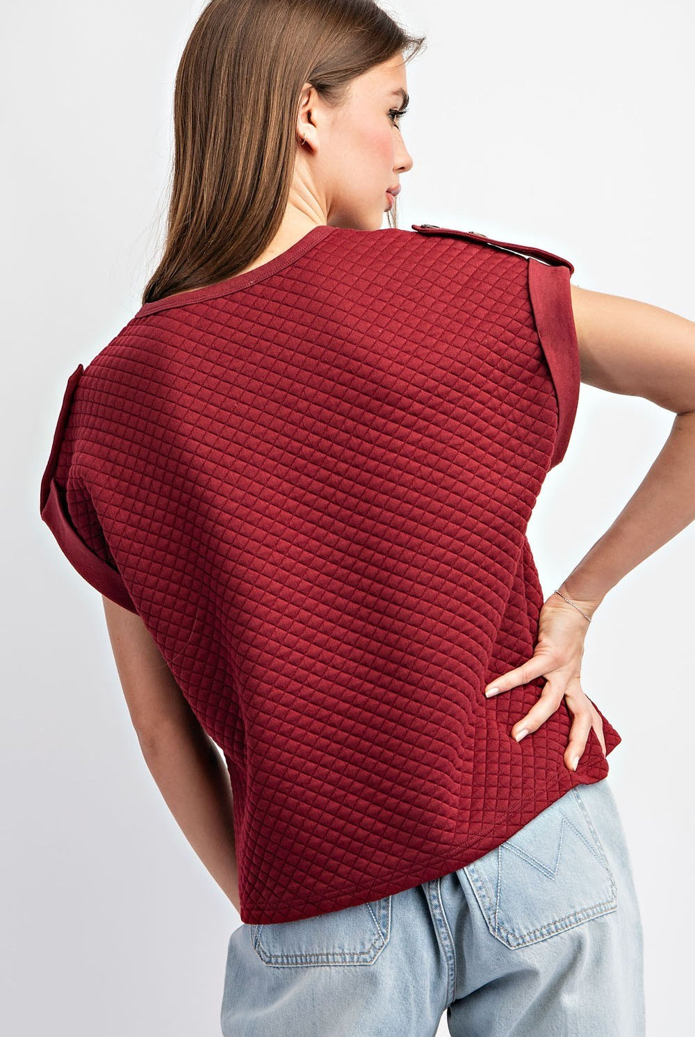 Woman wearing a textured red top and light blue jeans on a plain background