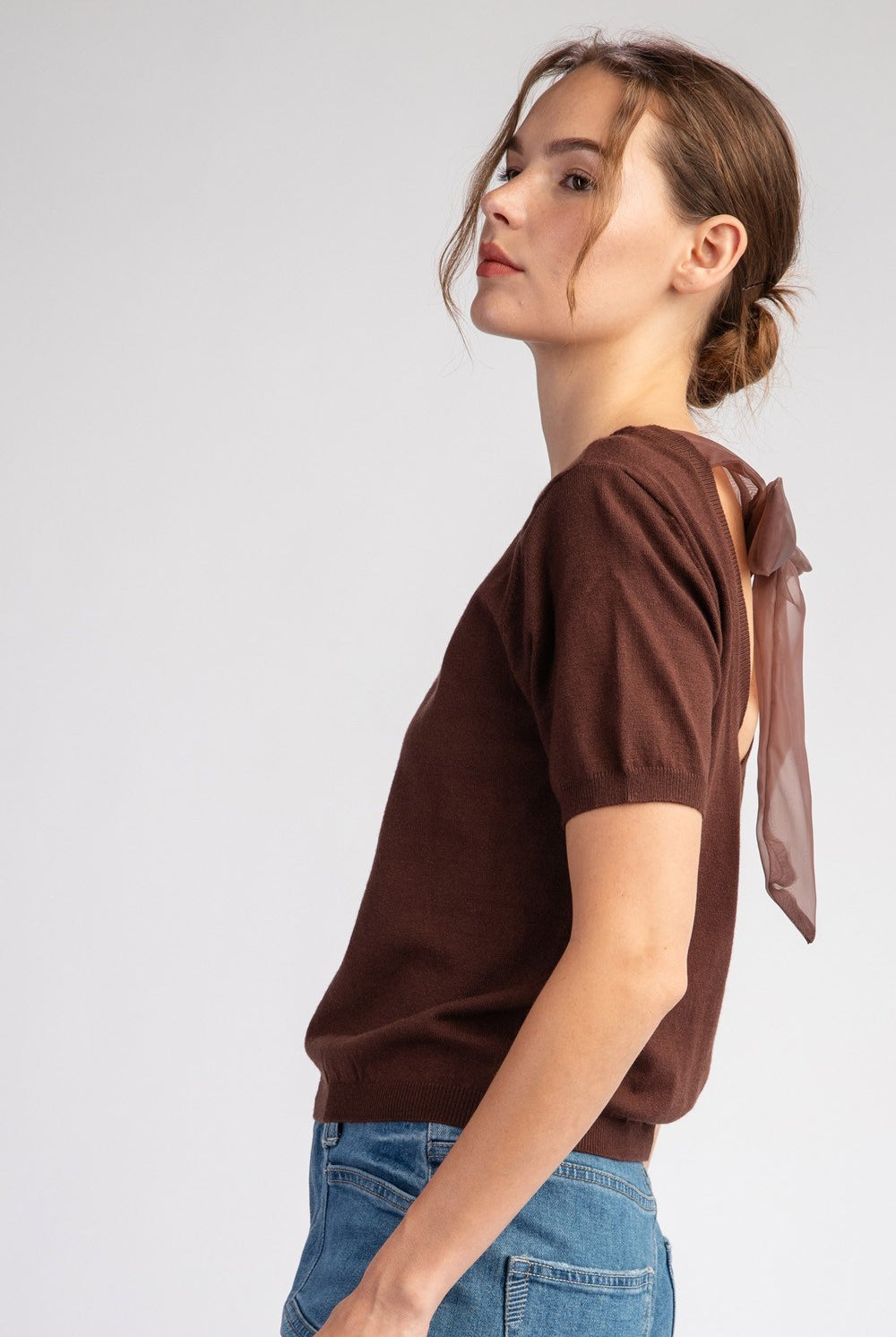 Woman wearing a brown t-shirt with a bow detail on a plain background