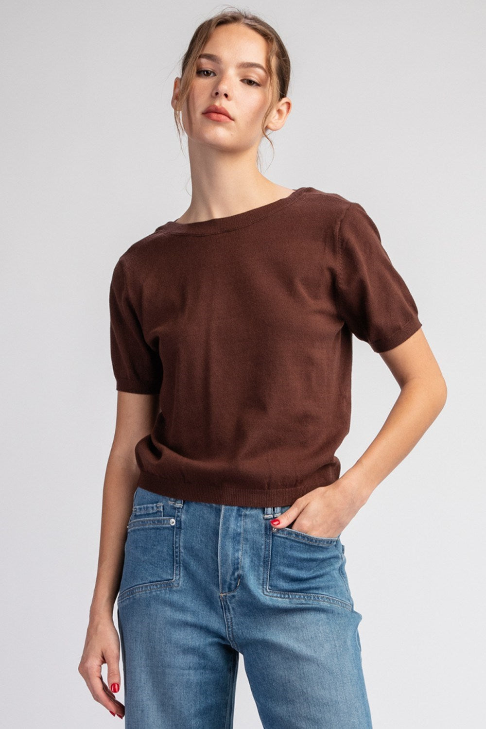 Woman wearing a brown top and blue jeans on a plain background