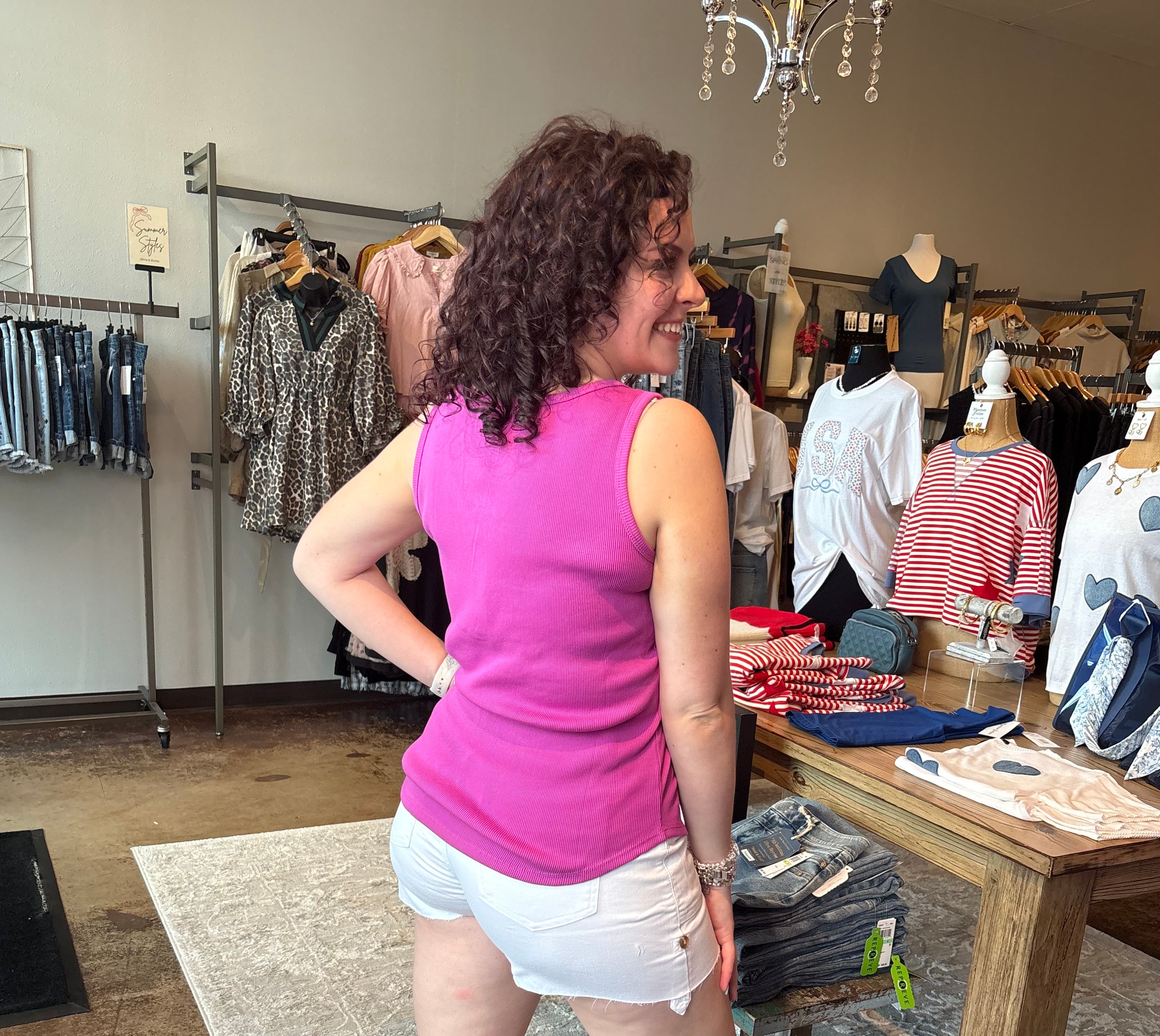 Woman in a pink top and white shorts standing in a store with clothes on racks.