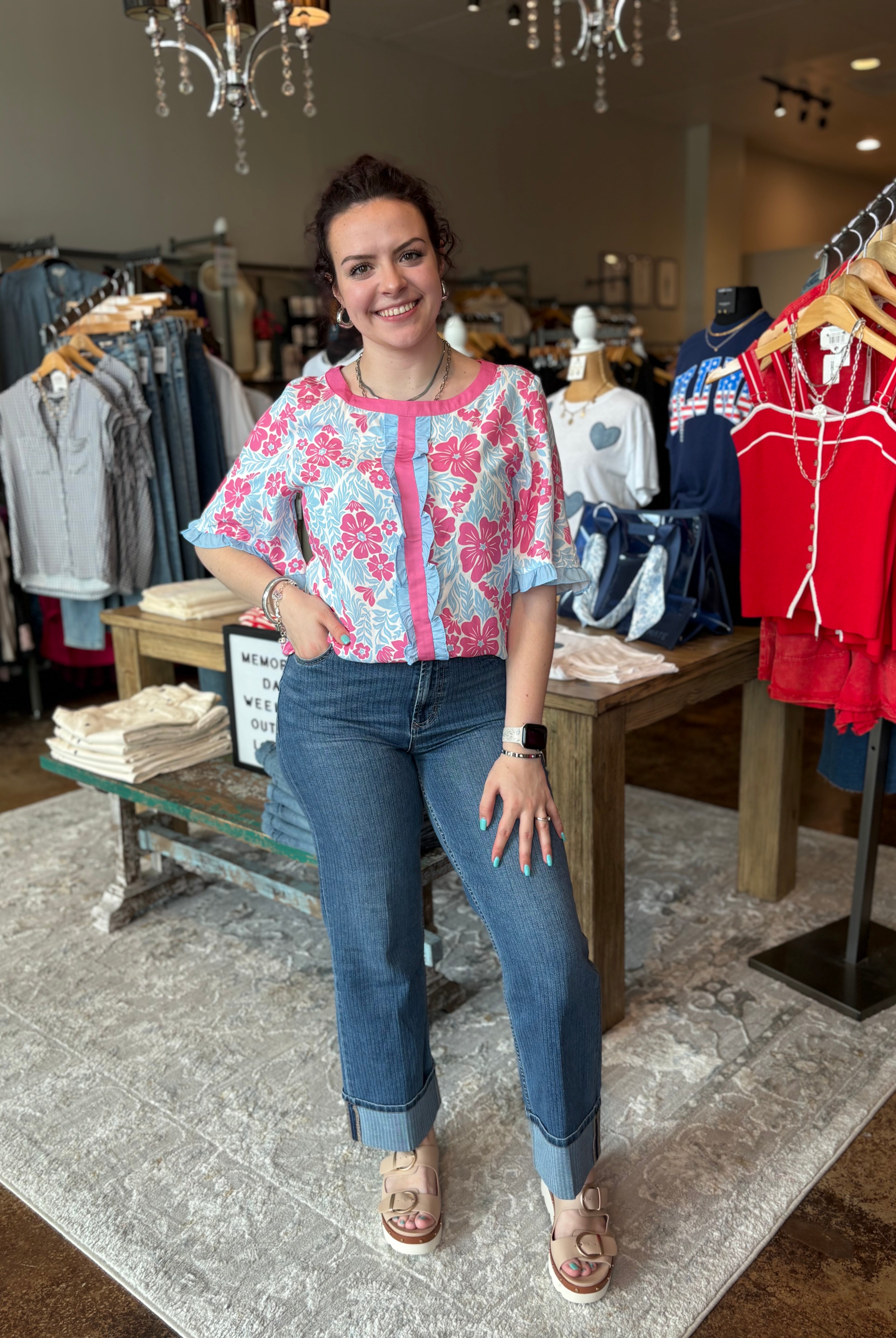 Woman in a floral top and jeans standing in a clothing store.