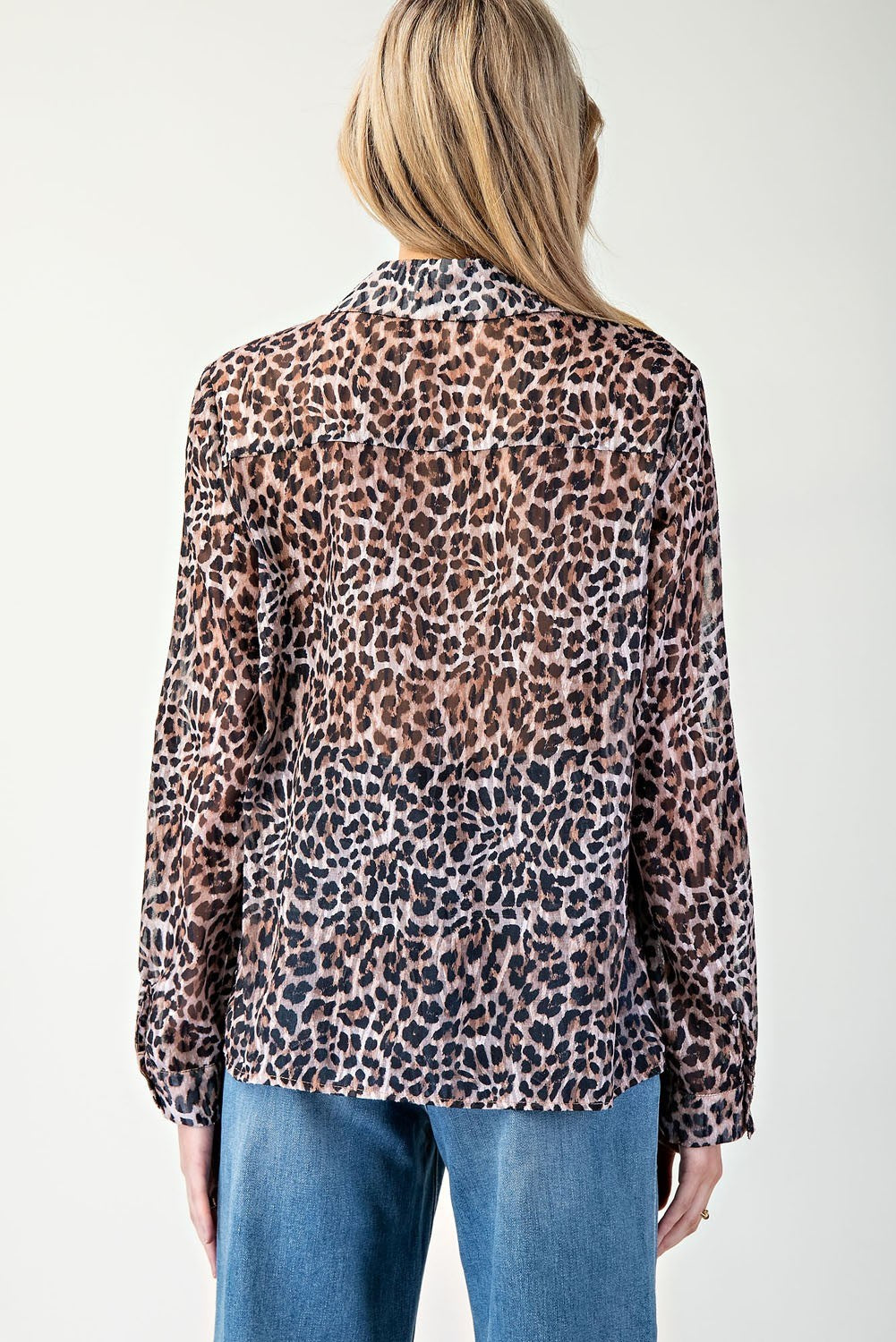Person wearing a leopard print blouse with blue jeans on a white background