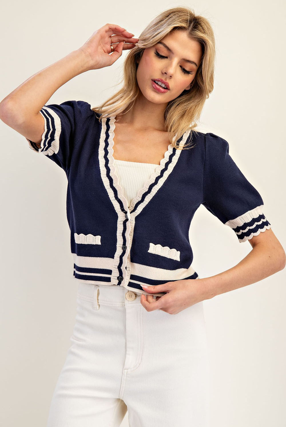 Woman wearing a navy cardigan with white trim on a plain background