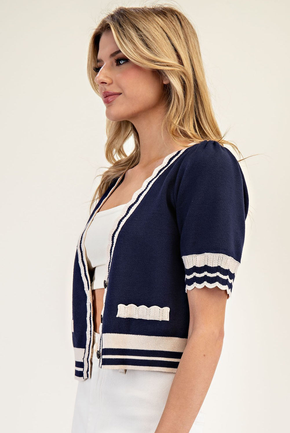 Woman wearing a navy cardigan with white accents on a plain background