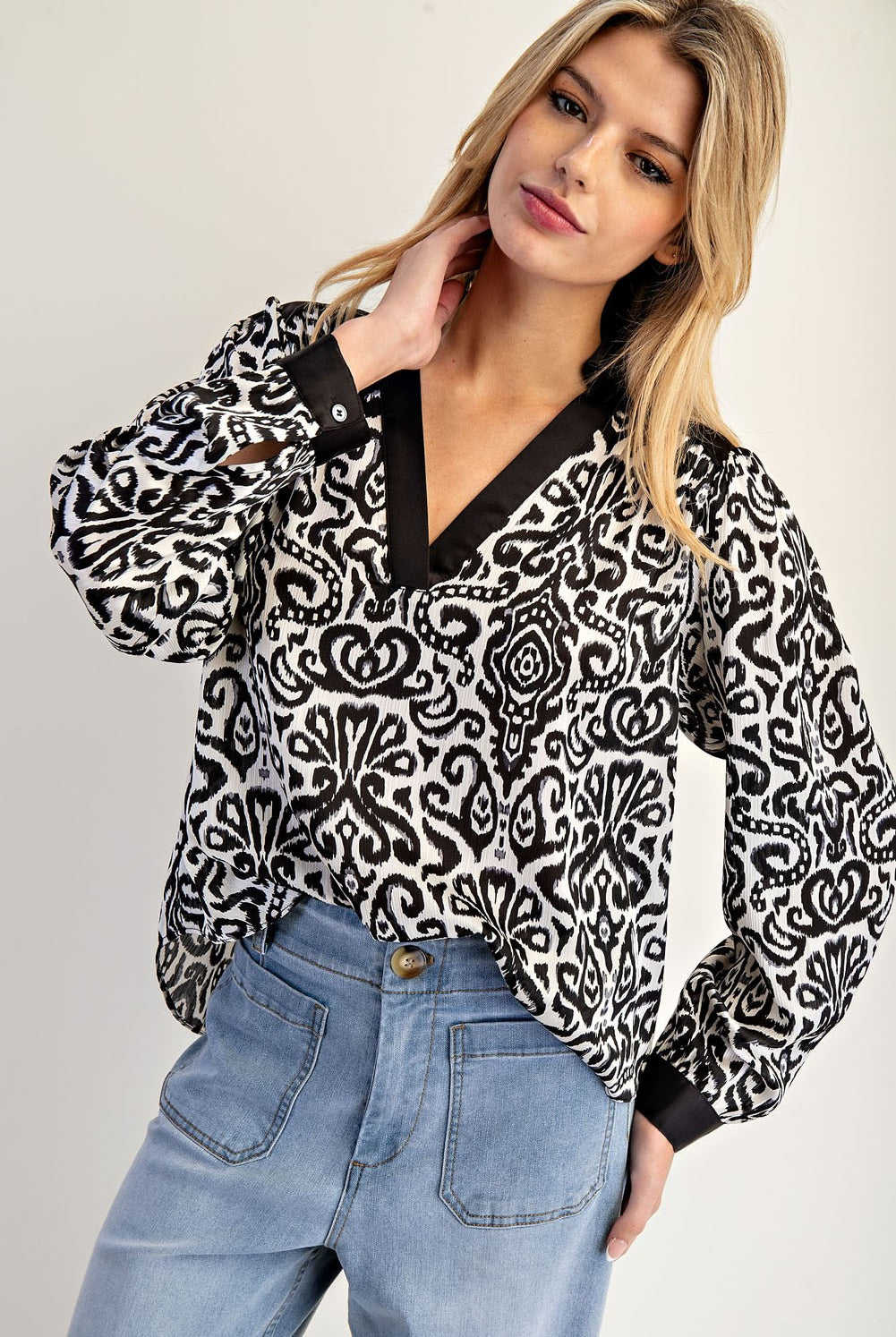 Woman wearing a black and white patterned blouse with blue jeans on a plain background