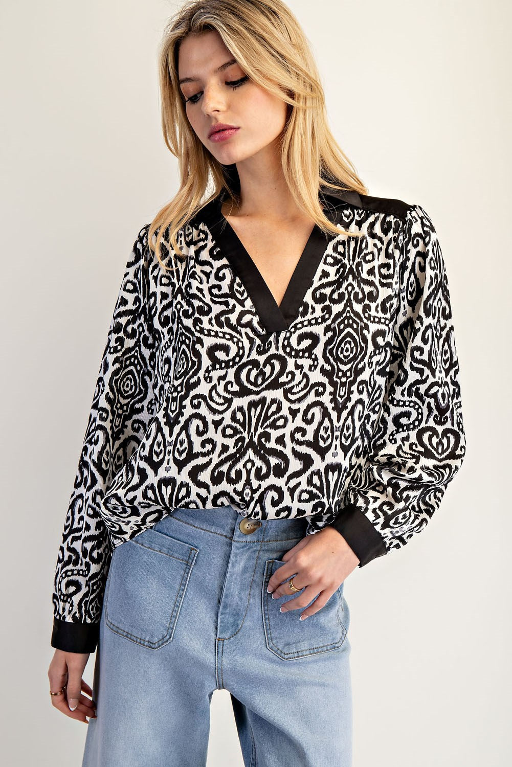 Woman wearing a black and white patterned blouse with blue jeans on a plain background