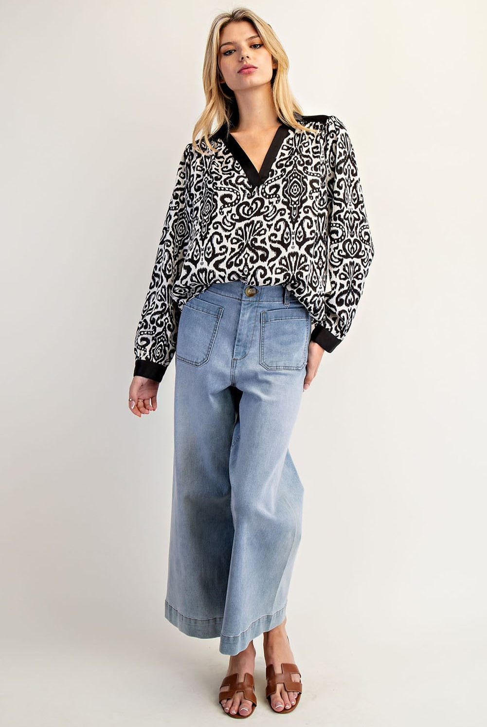 Woman wearing a black and white patterned blouse and light blue jeans on a white background