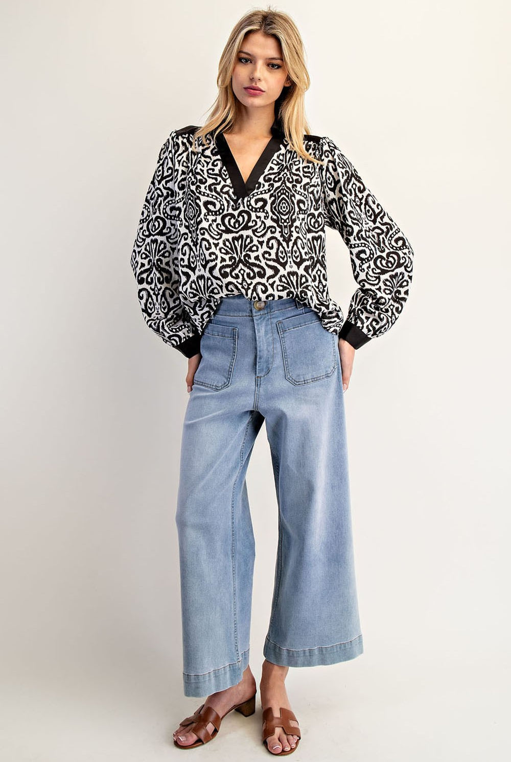 Woman wearing a black and white patterned blouse and light blue jeans on a white background
