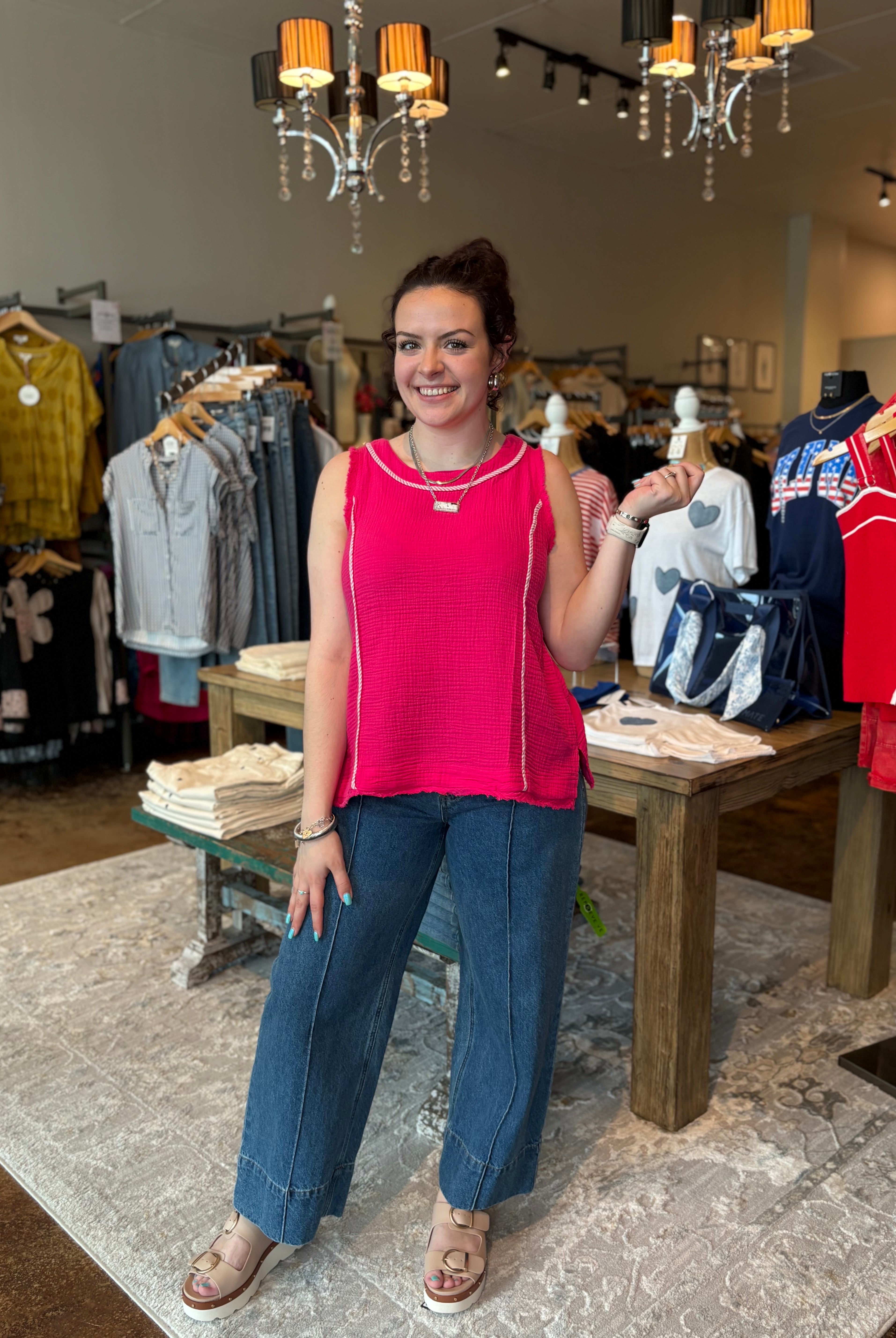 Woman in a bright pink sleeveless top and blue jeans standing in a clothing store.