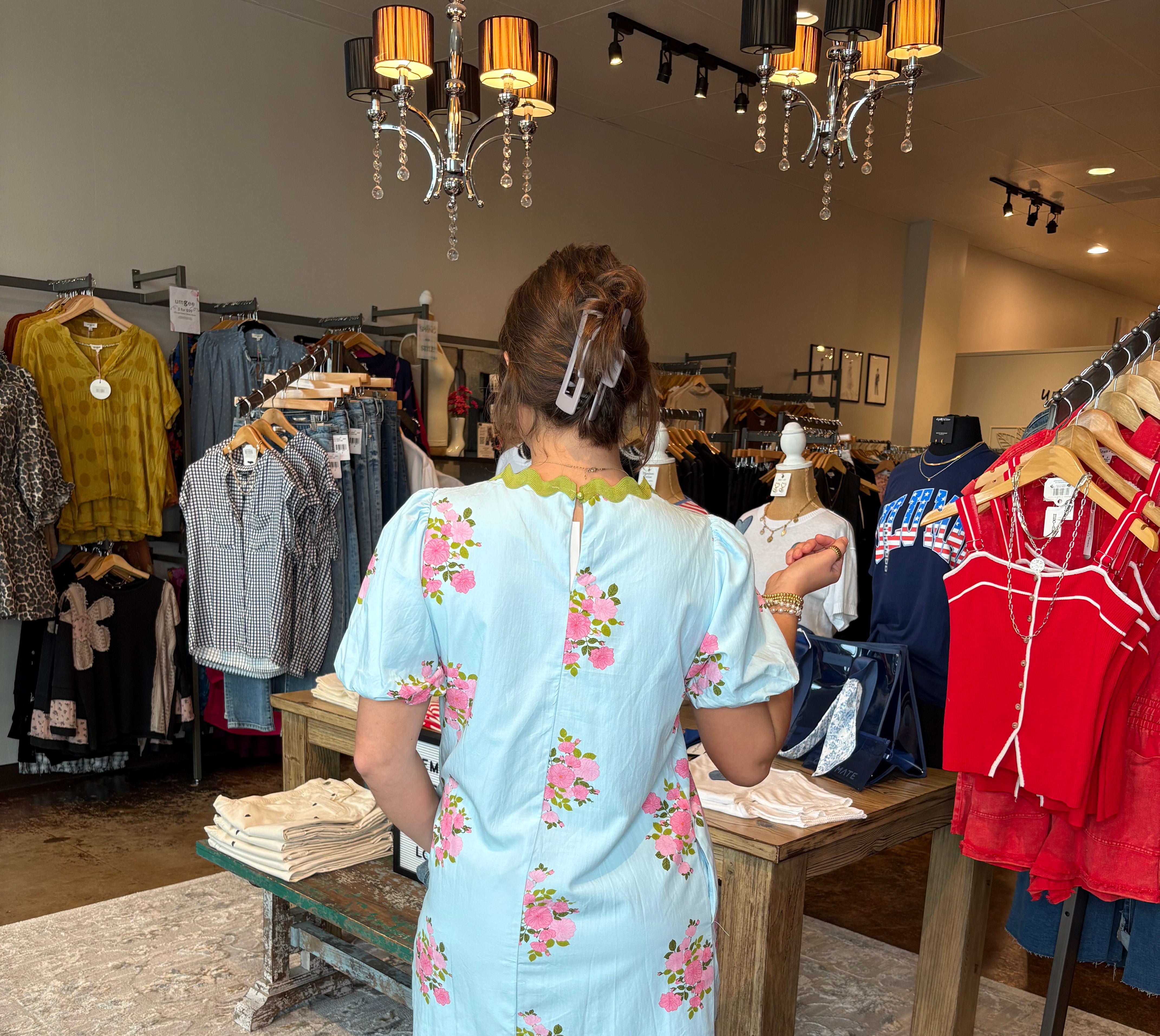 Person wearing a floral dress standing in a store with clothing racks and displays.