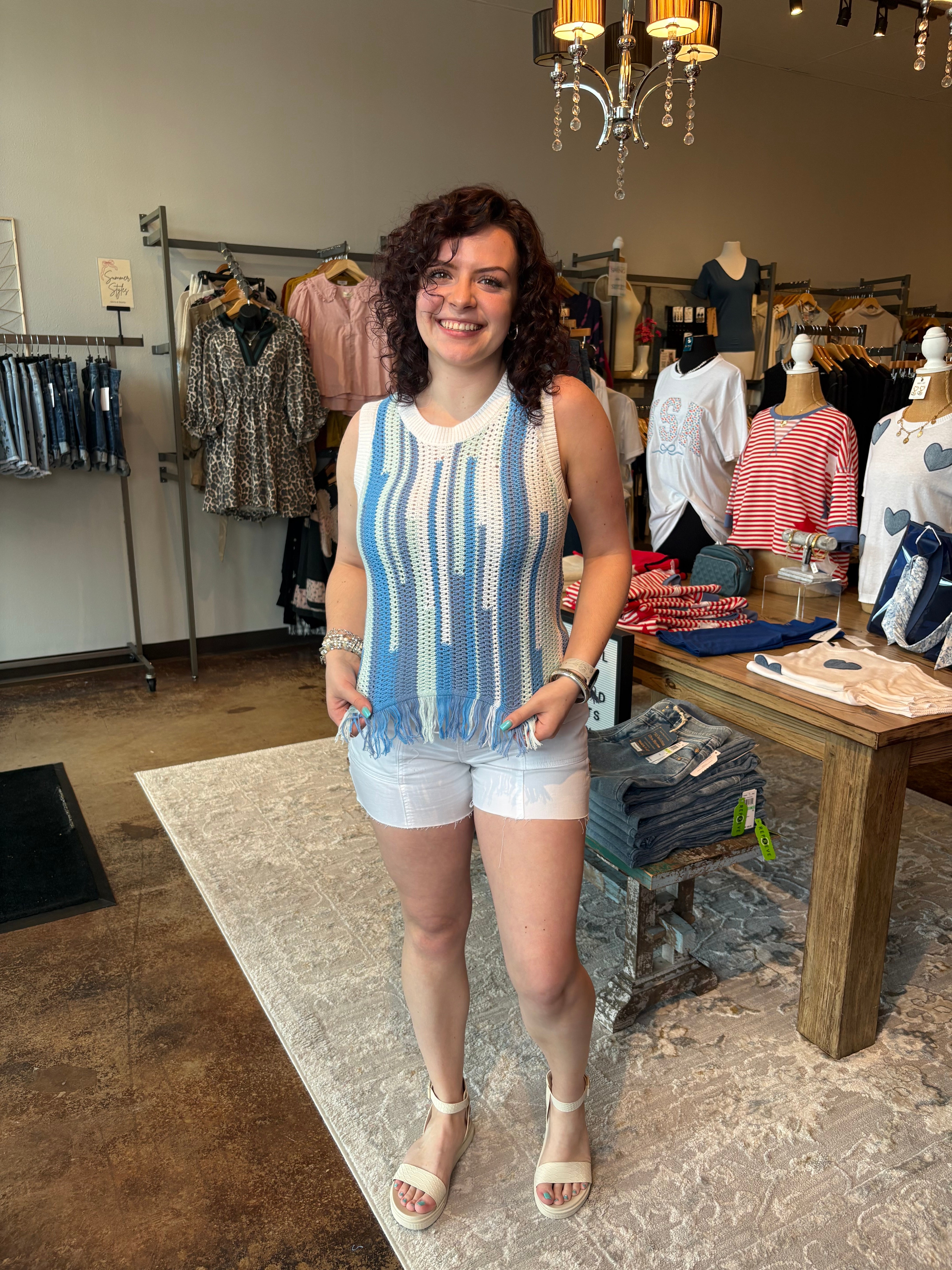 Woman standing in a clothing store wearing a blue and white striped sleeveless top and white shorts.