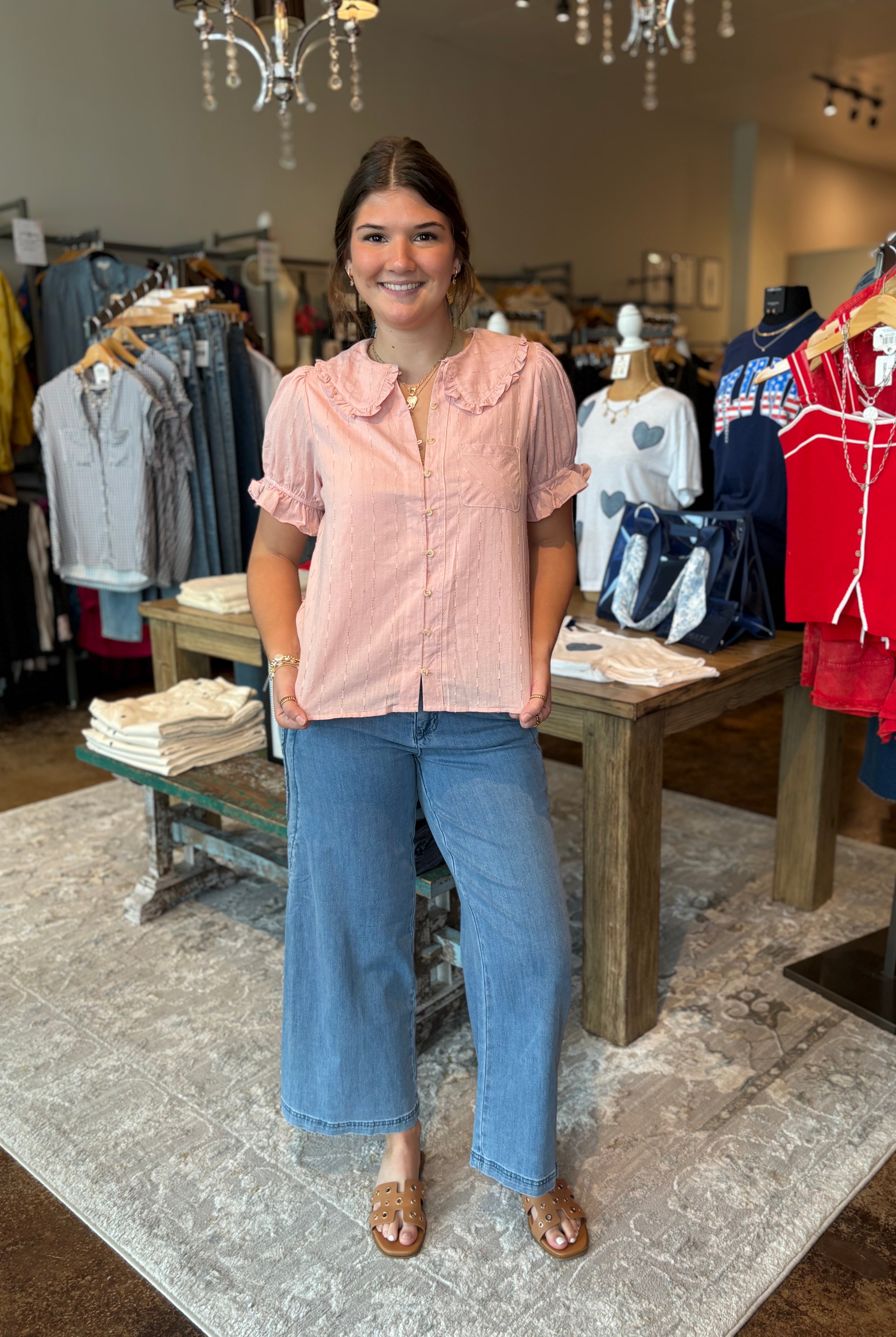 Woman in a pink blouse and blue jeans standing in a clothing store.