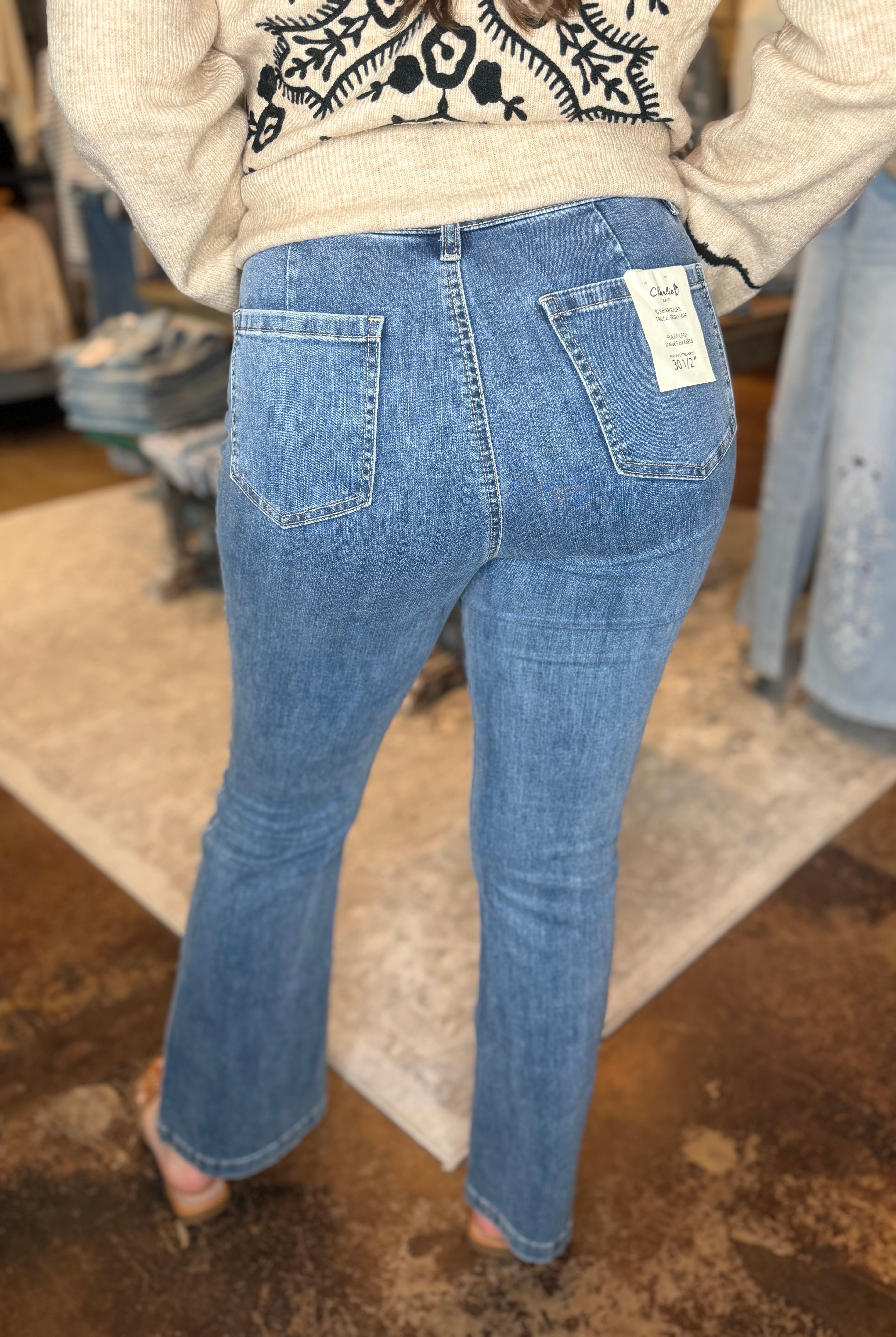 A person shown from the back wearing light blue denim jeans with a visible white size tag on the back pocket, standing in a clothing store.