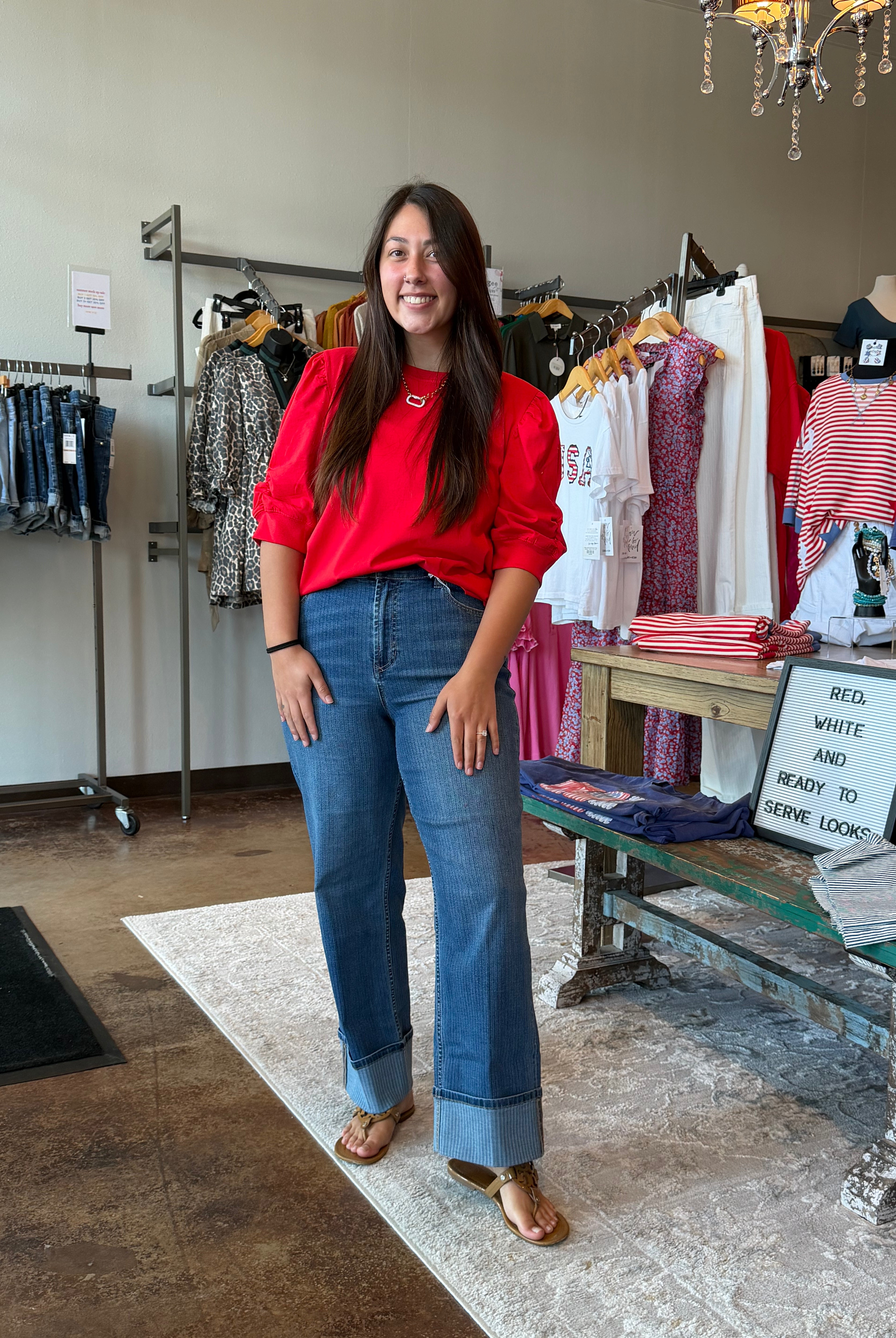Woman in a red shirt and blue jeans standing in a clothing store.