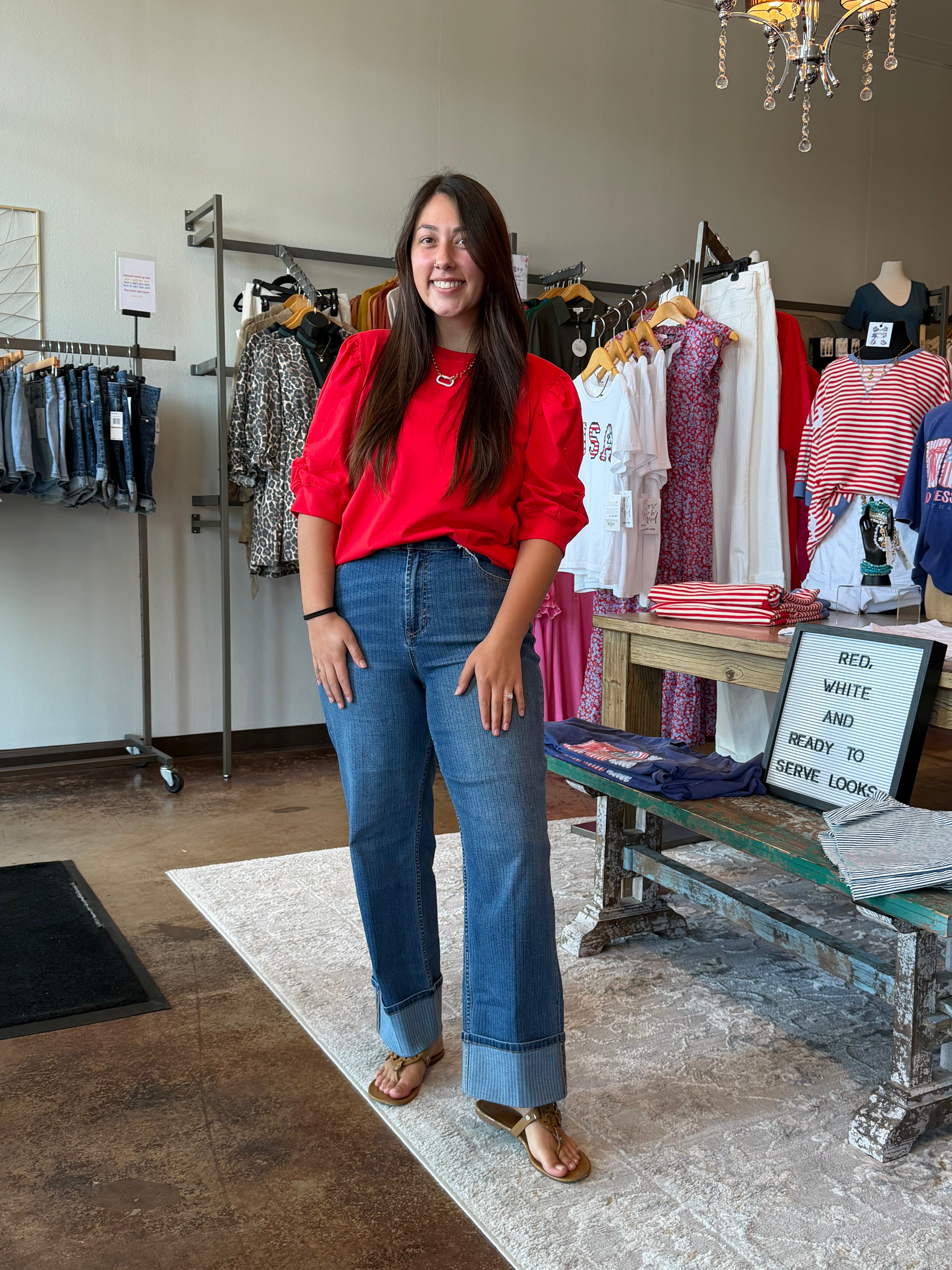 Woman in a red shirt and blue jeans standing in a clothing store.