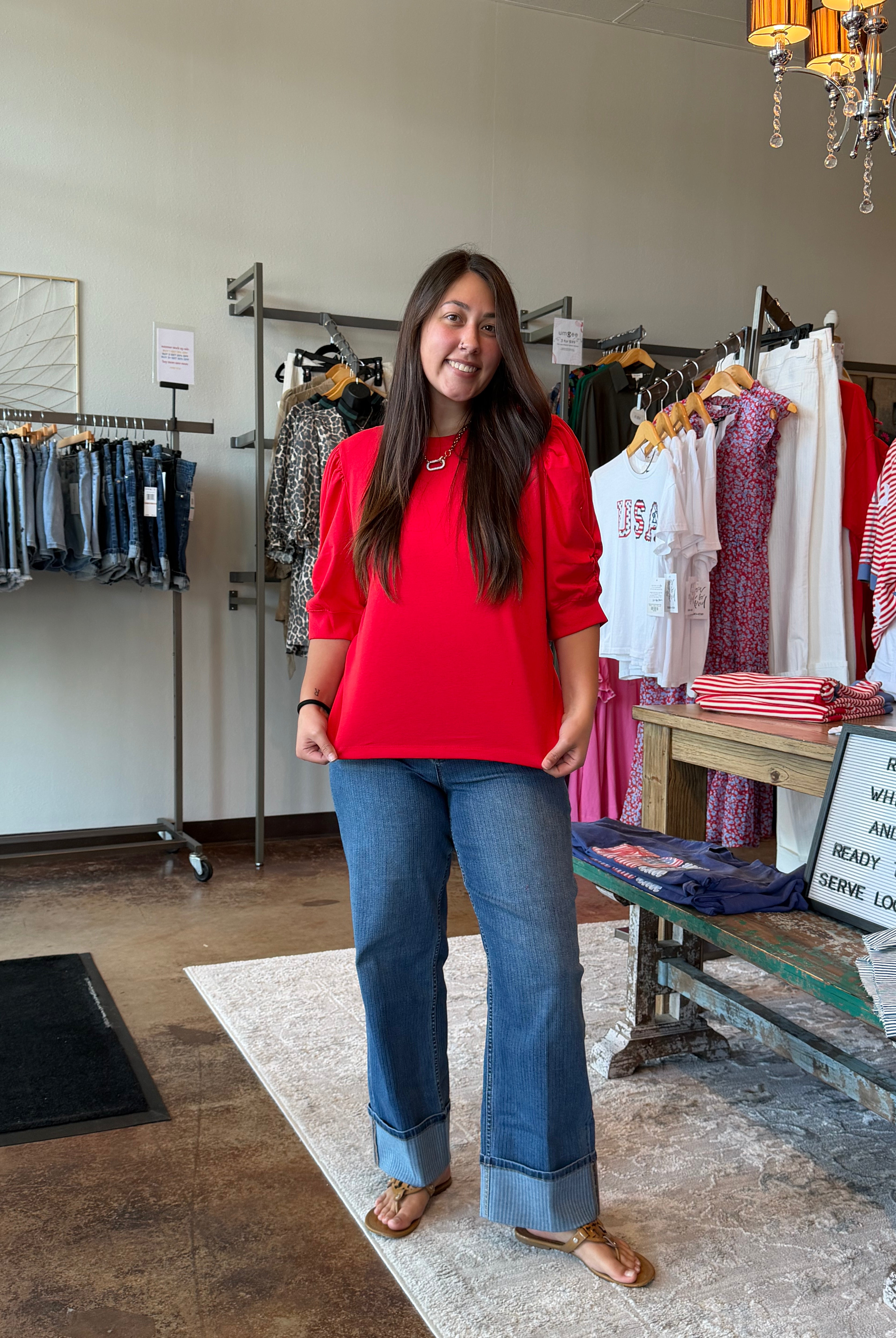 Woman in a red shirt and blue jeans standing in a clothing store.