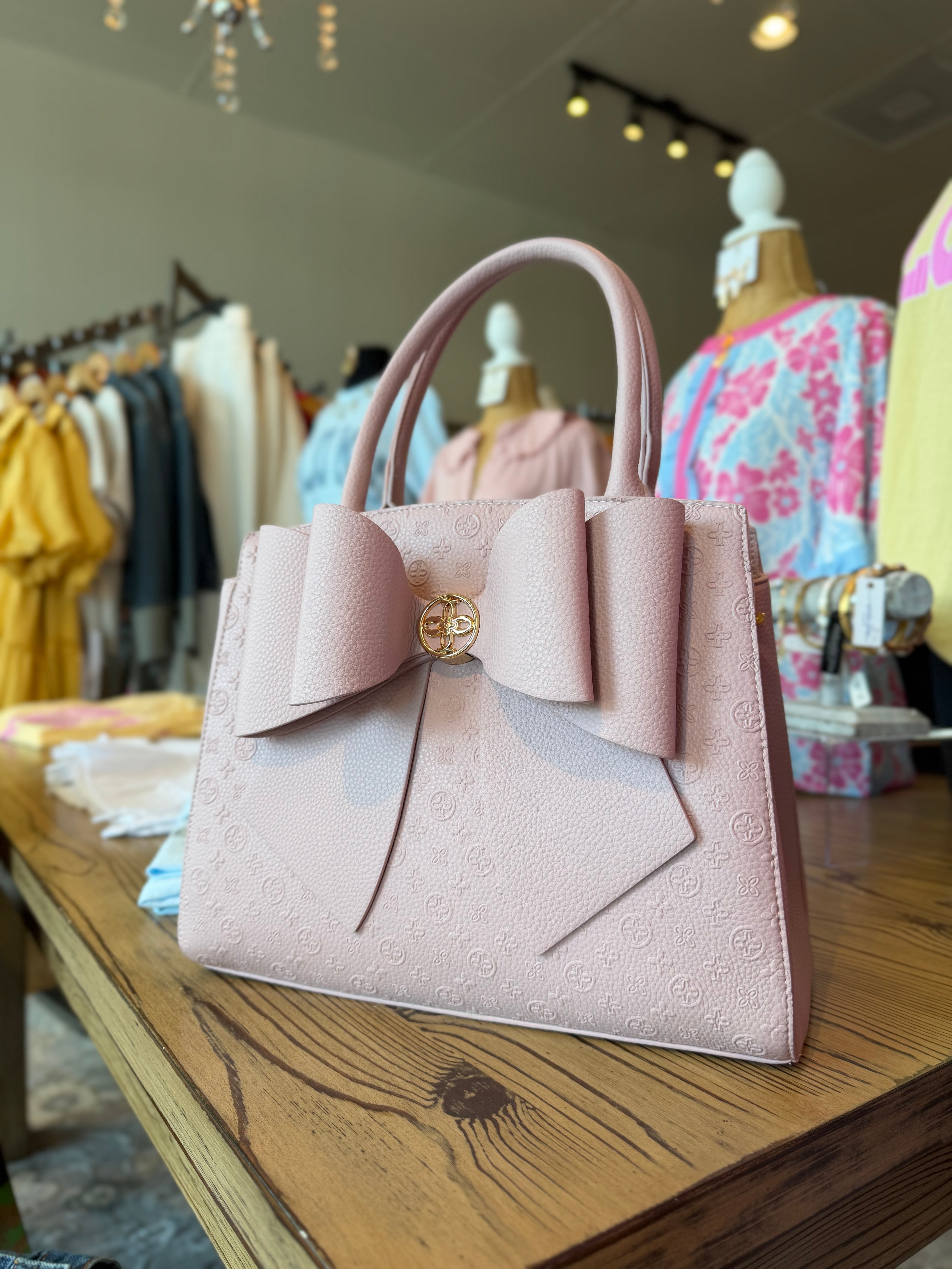 Pink handbag with a bow detail on a wooden table in a clothing store.