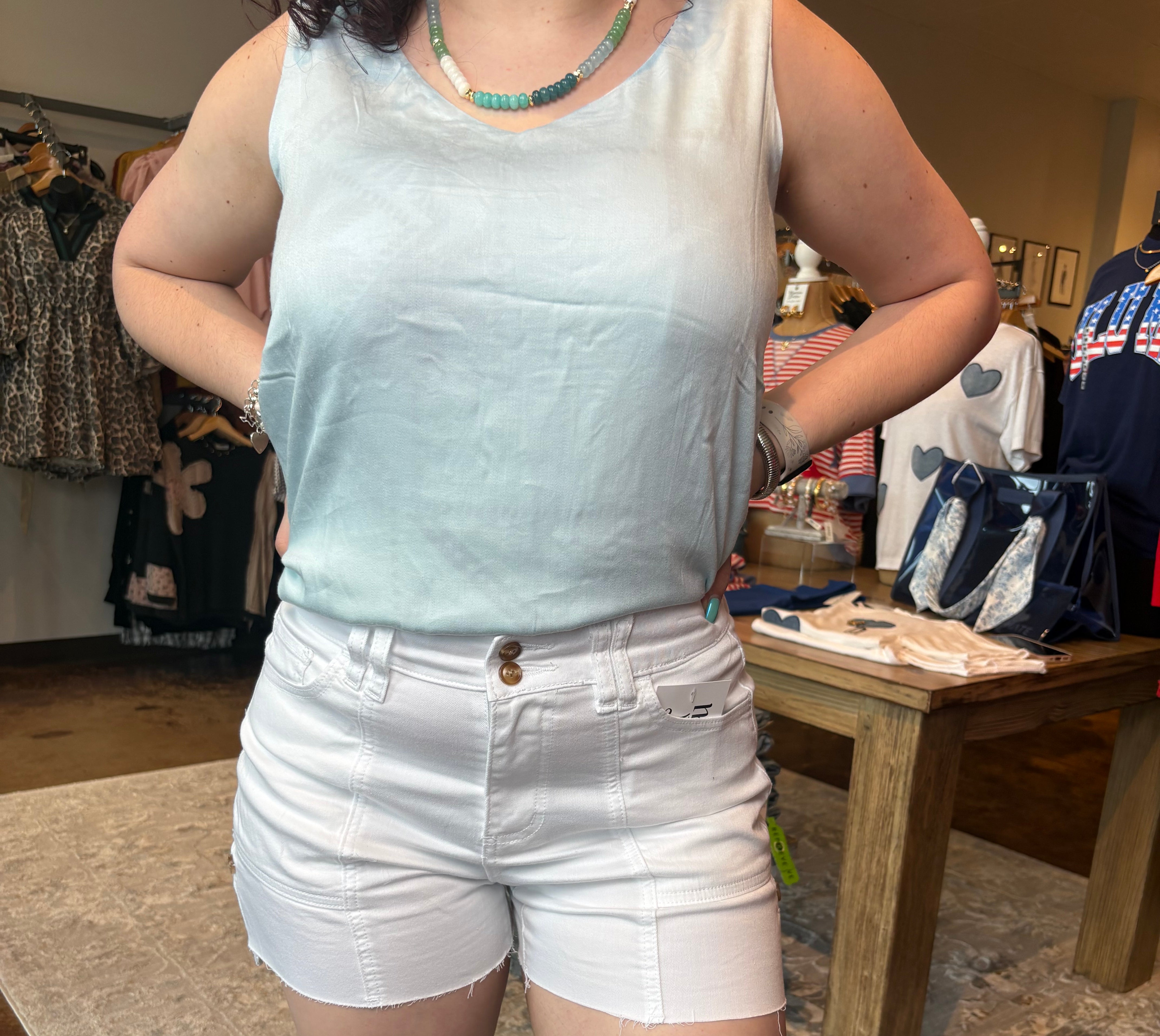 Person wearing a white sleeveless top and shorts in an indoor setting with furniture and boxes.