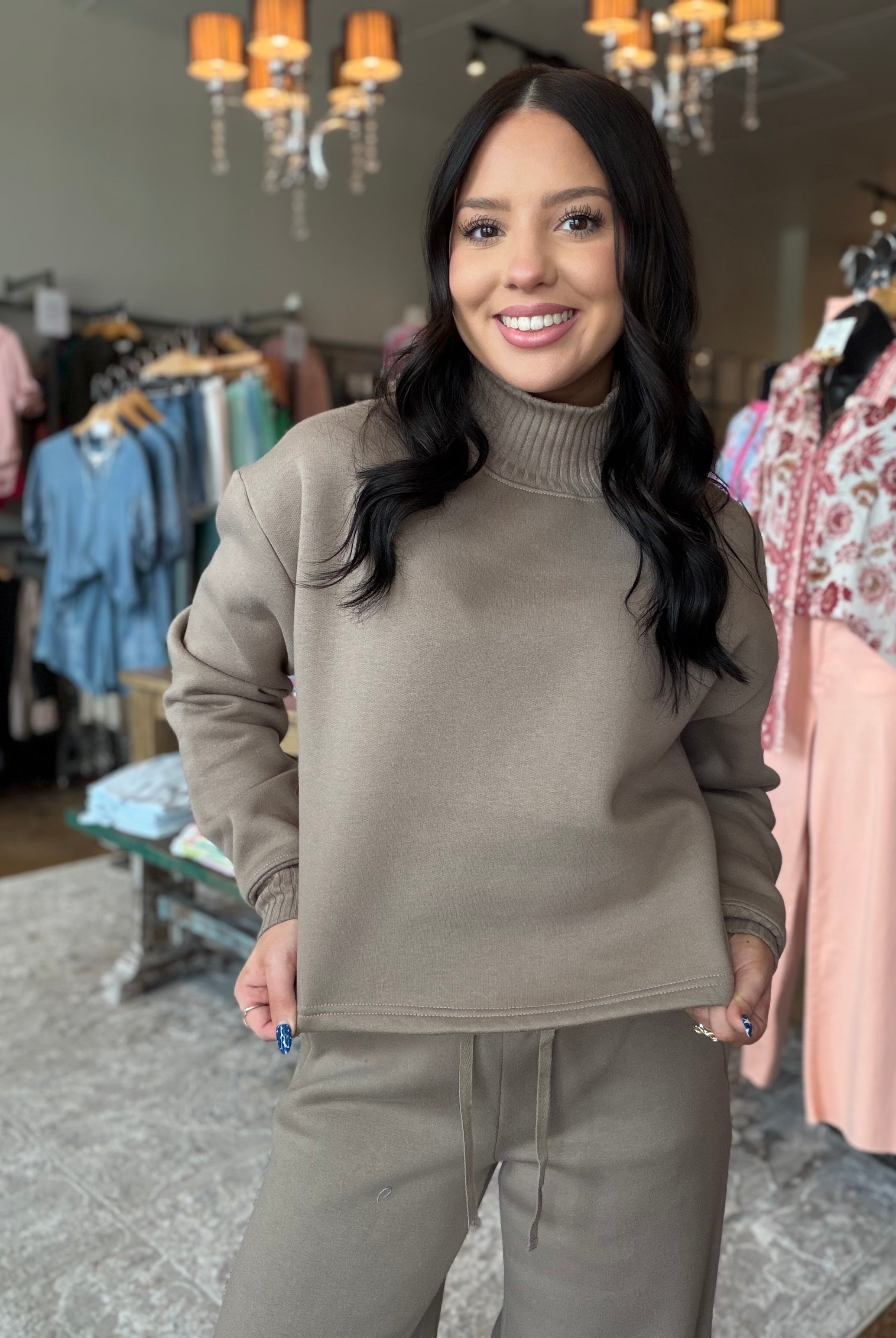 A woman modeling a taupe brown ribbed mock neck sweatshirt and matching sweatpants in a boutique clothing store.