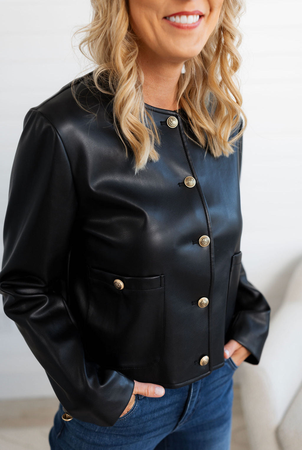 Woman wearing a black leather jacket with gold buttons against a white background