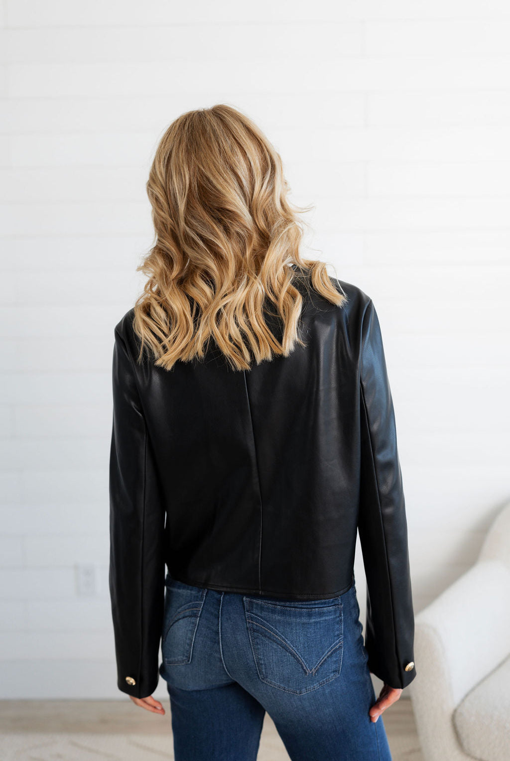 Person wearing a black leather jacket and blue jeans against a white wall.