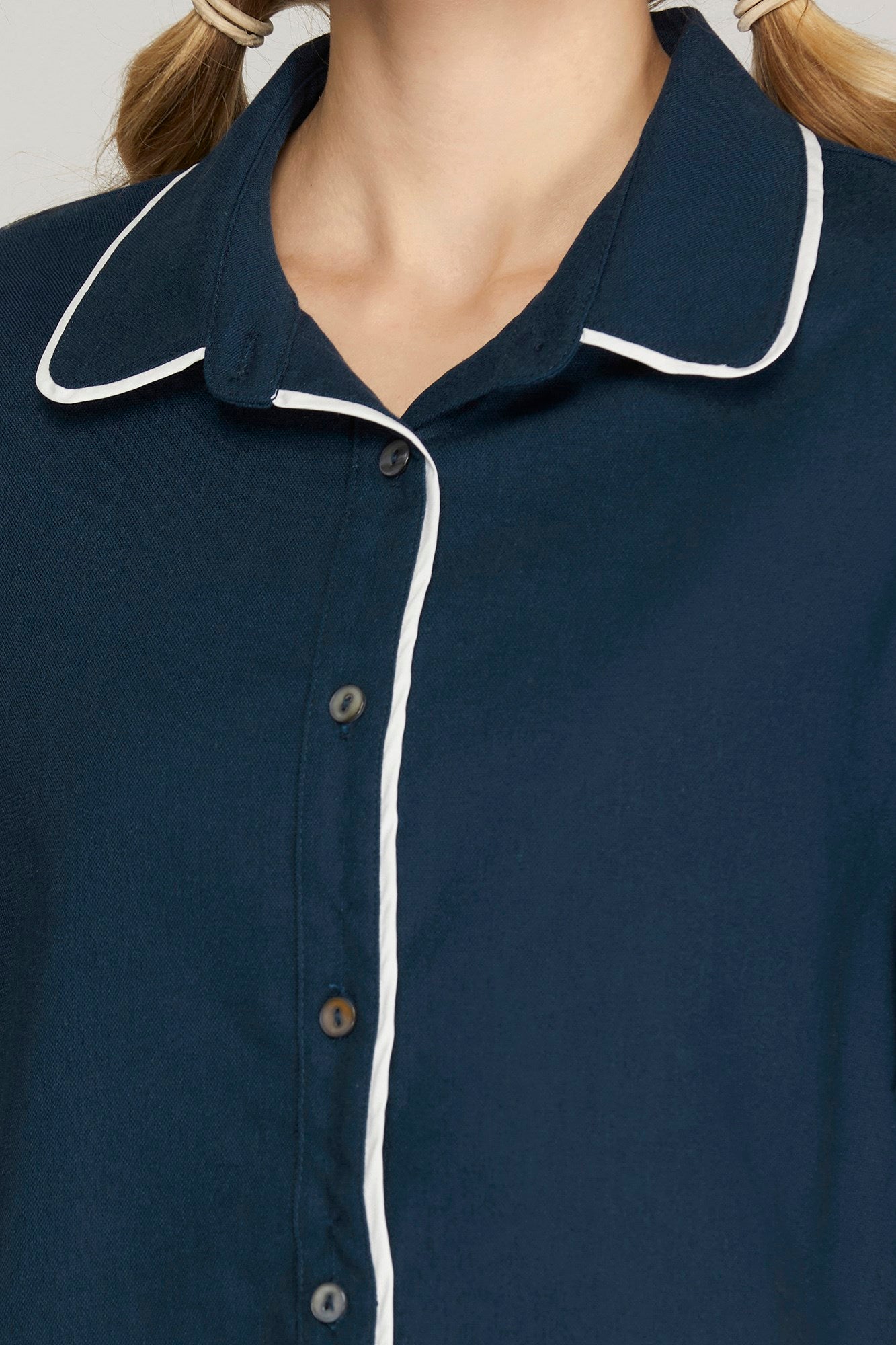 Close-up of a navy blue button-up shirt with white piping trim on the collar and front placket, worn by a model with blonde pigtails.