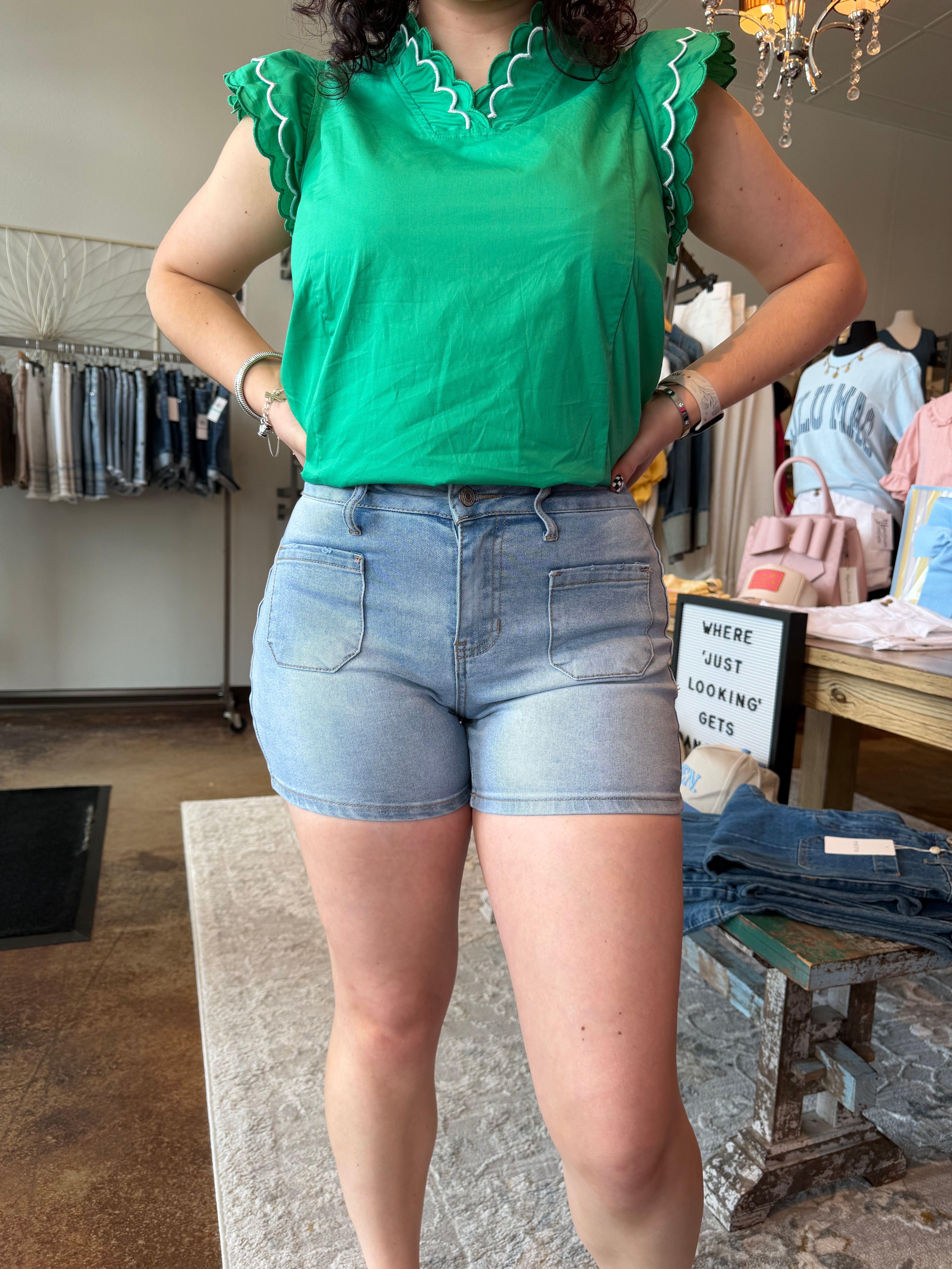 Person wearing a green top with ruffled sleeves and blue shorts in a store setting.