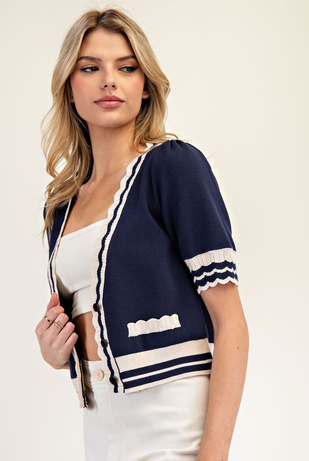 Woman wearing a navy cardigan with white trim on a plain background