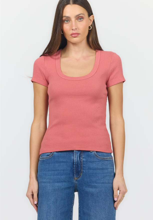 A woman modeling a short-sleeve scoop-neck ribbed knit top in dusty rose pink, paired with blue jeans, against a light gray studio background.
