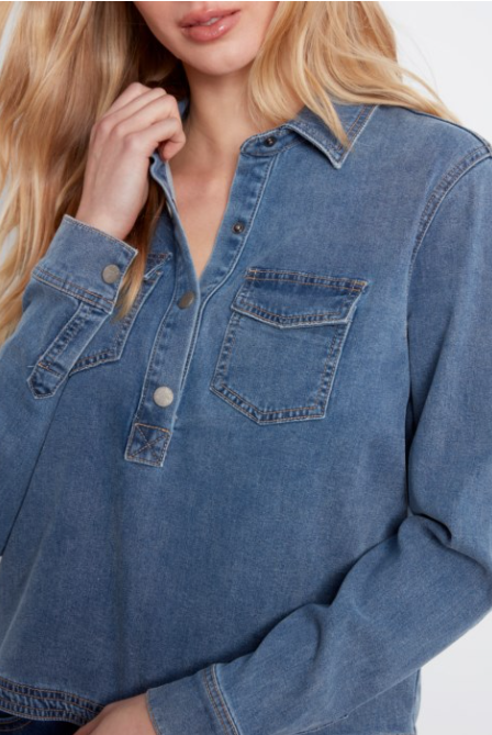 A close-up of a woman wearing a blue denim long-sleeve button-up shirt with chest pockets, shown against a plain light background.
