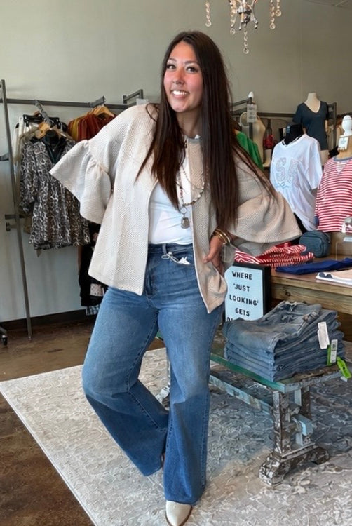 Woman posing in a clothing store wearing a beige jacket and blue jeans.