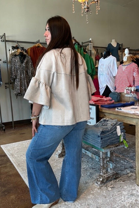 Woman in a beige jacket and blue jeans standing in a clothing store.
